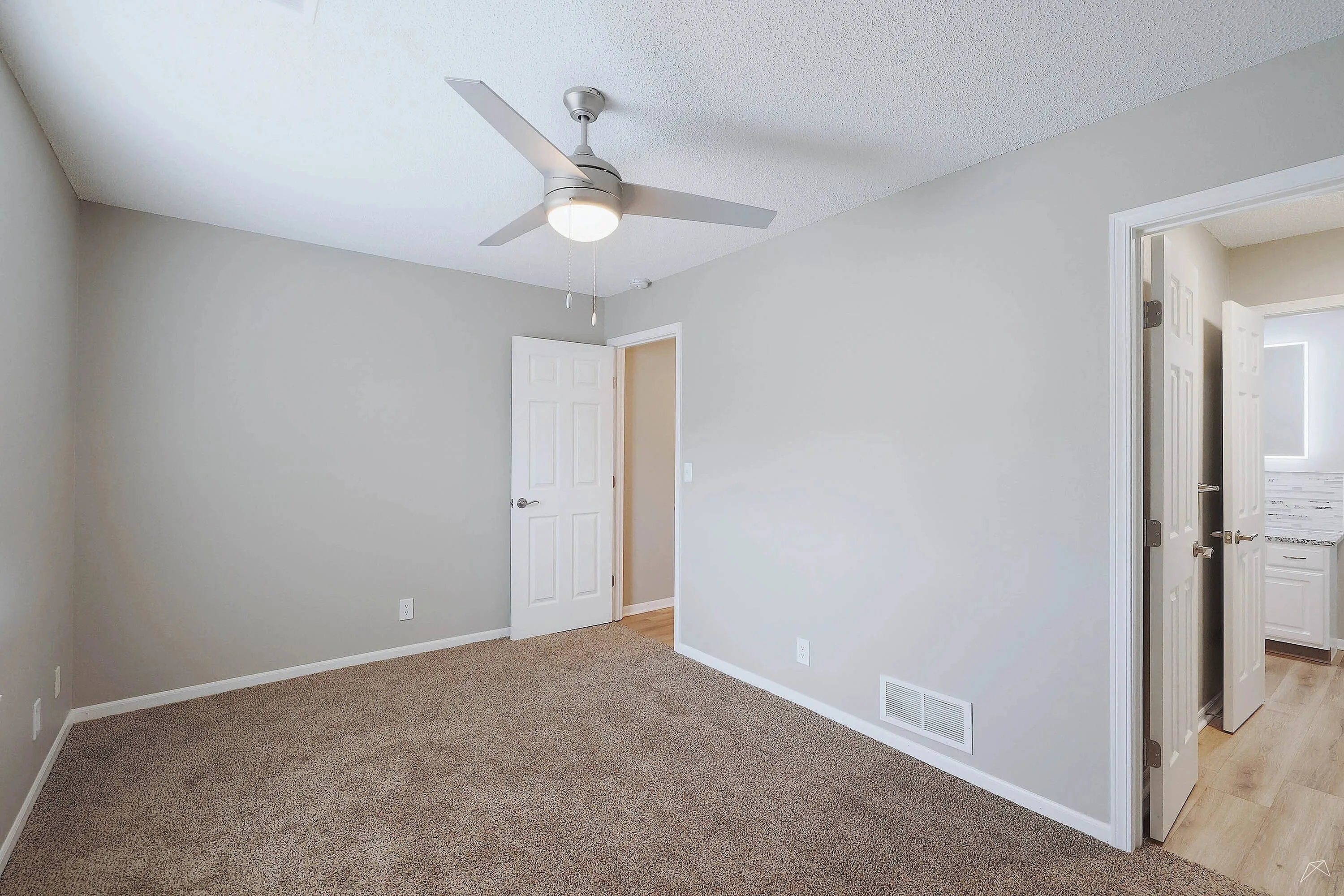 Inviting bedroom with soft carpeting, modern ceiling fan, and an open doorway leading to a stylish bathroom.