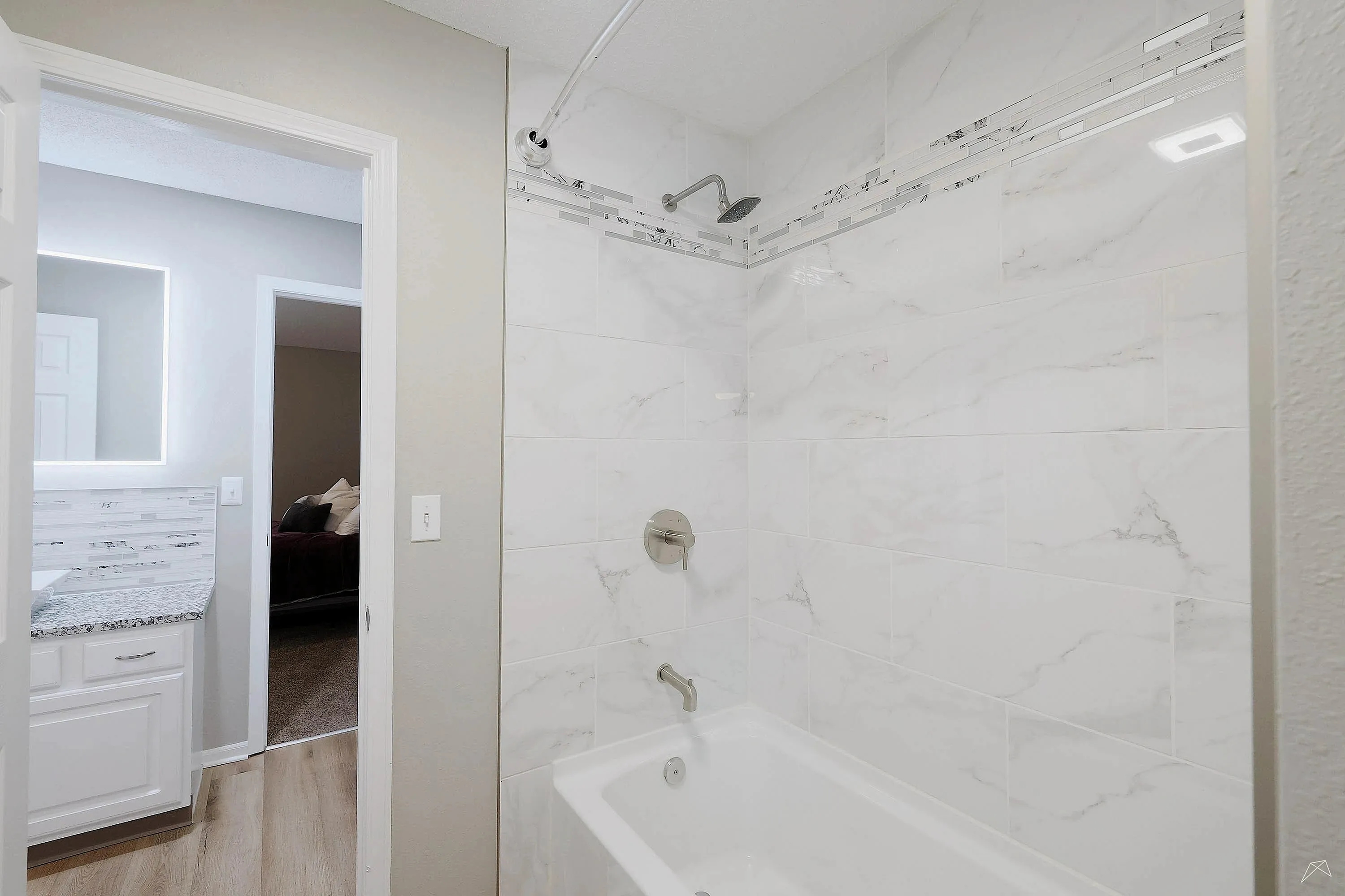 Elegant bathroom showcasing modern white marble tile, a chic bathtub, and a sleek vanity with illuminated mirror, enhancing the sophisticated ambiance.