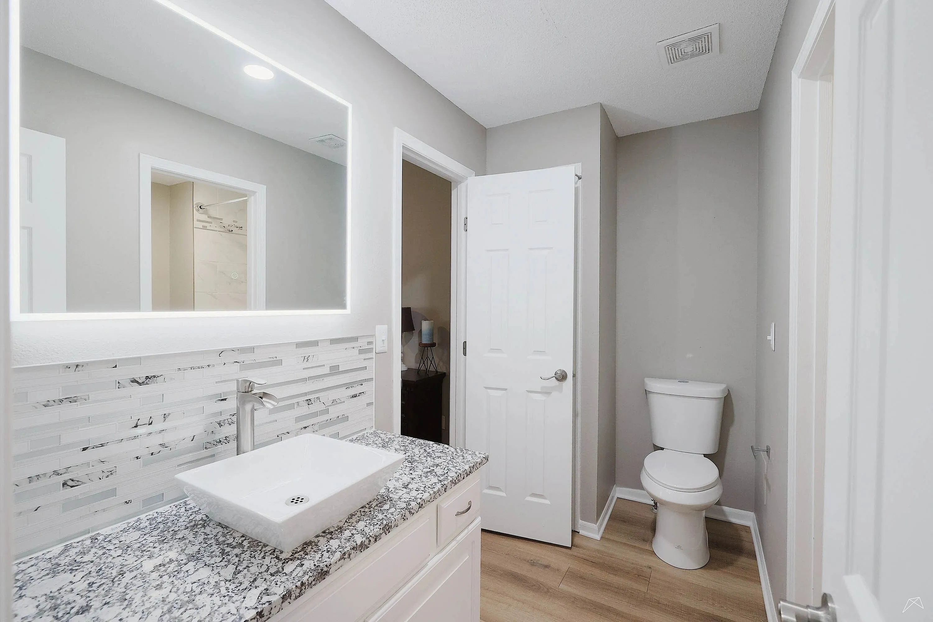 Elegant bathroom featuring a modern vanity with granite countertop, stylish backsplash, and illuminated mirror.