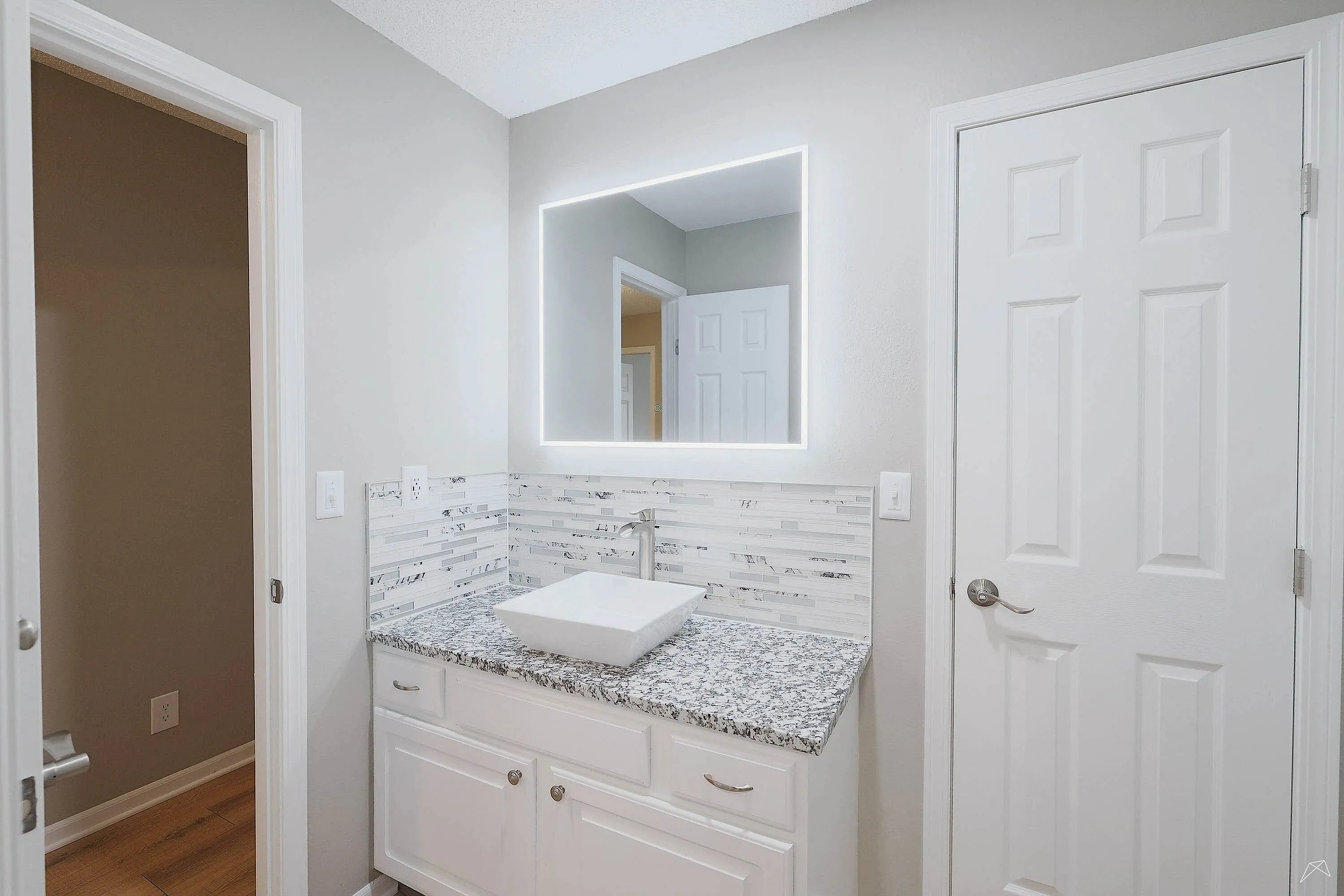 Modern bathroom featuring an illuminated mirror, elegant gray granite countertop, and stylish white cabinetry.