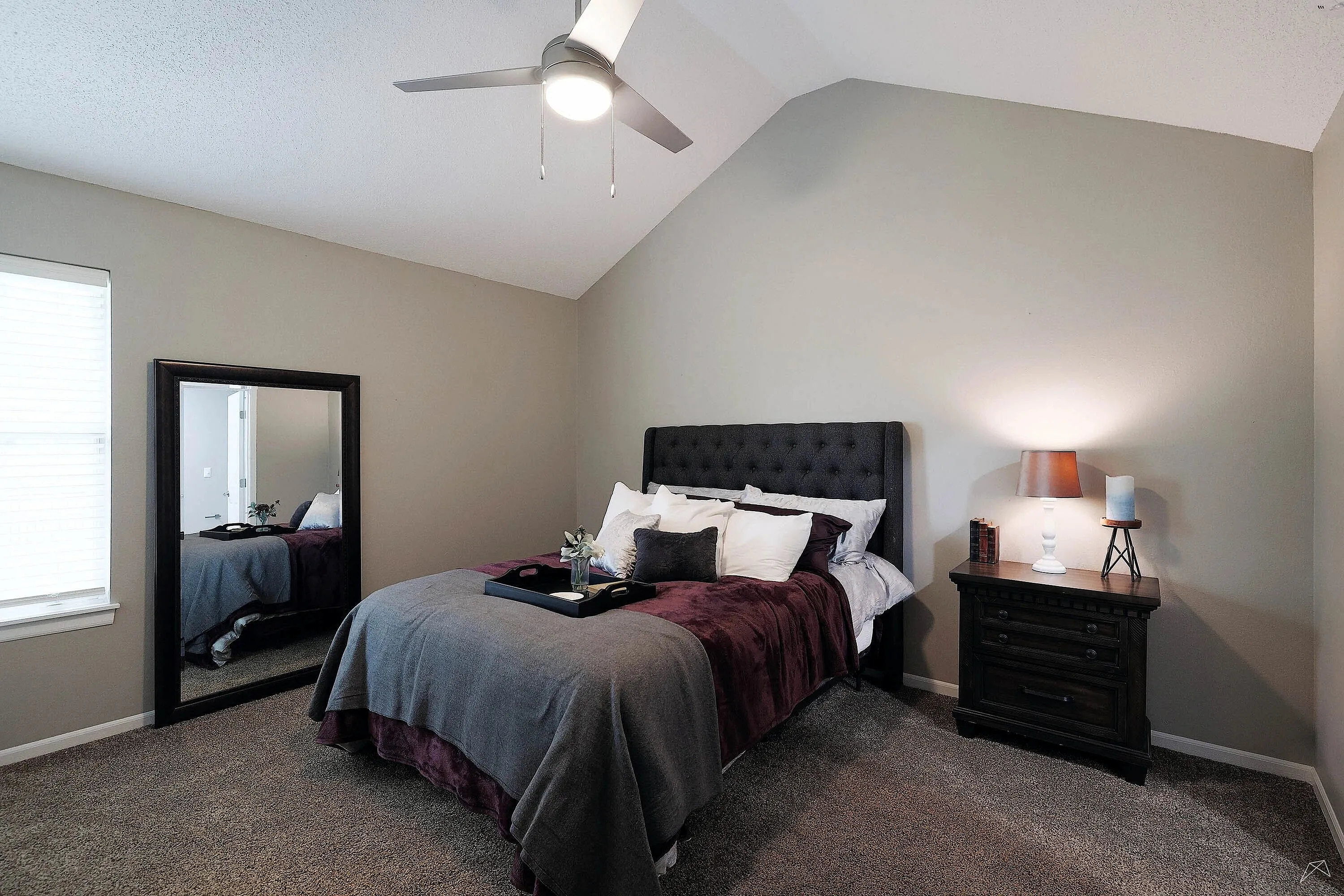 Inviting bedroom with vaulted ceiling, elegant tufted headboard, plush pillows, and a cozy ambiance.