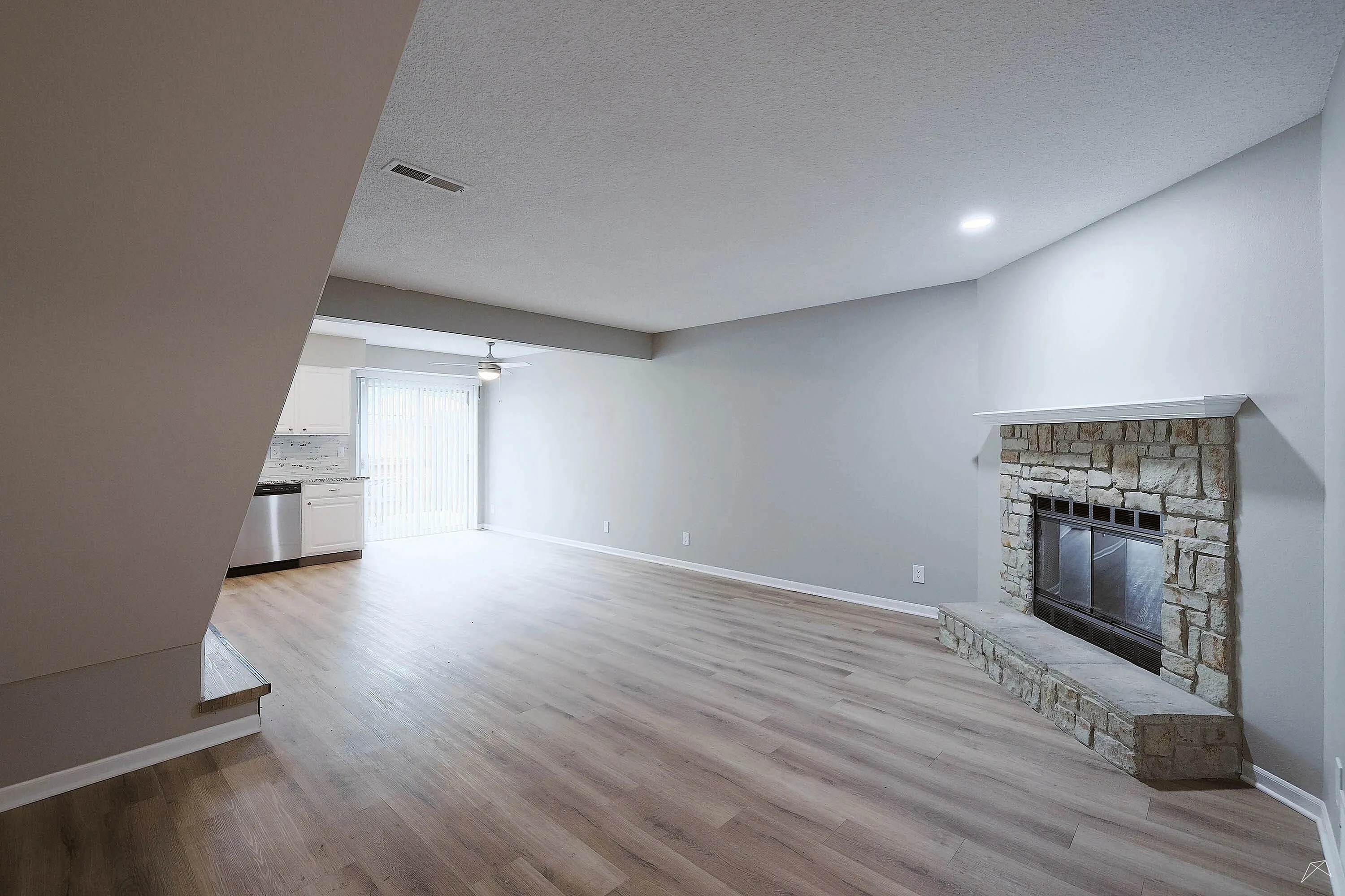 Bright and spacious living area with elegant wooden flooring, stone fireplace, and modern kitchen design.