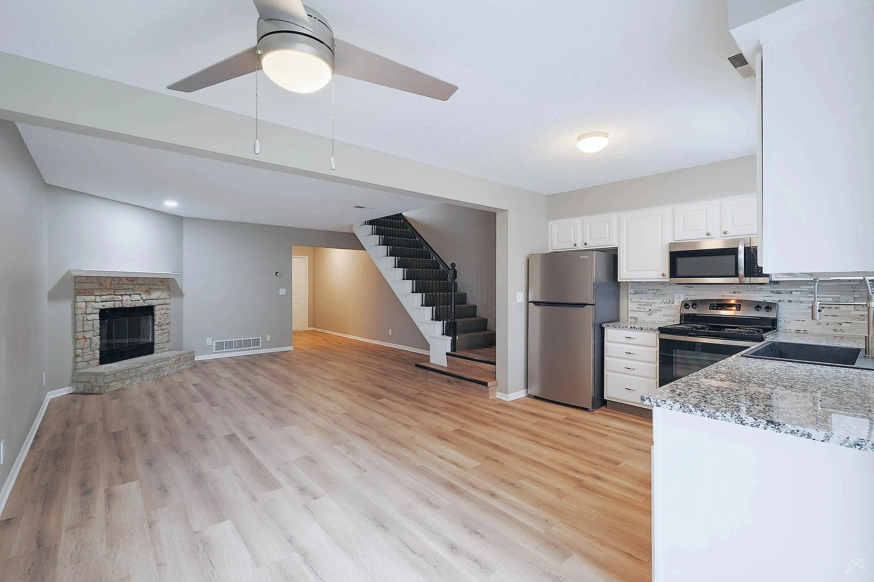 Chic open-concept living area featuring sleek laminate flooring, a cozy stone fireplace, modern kitchen with granite countertops, and elegant staircase.