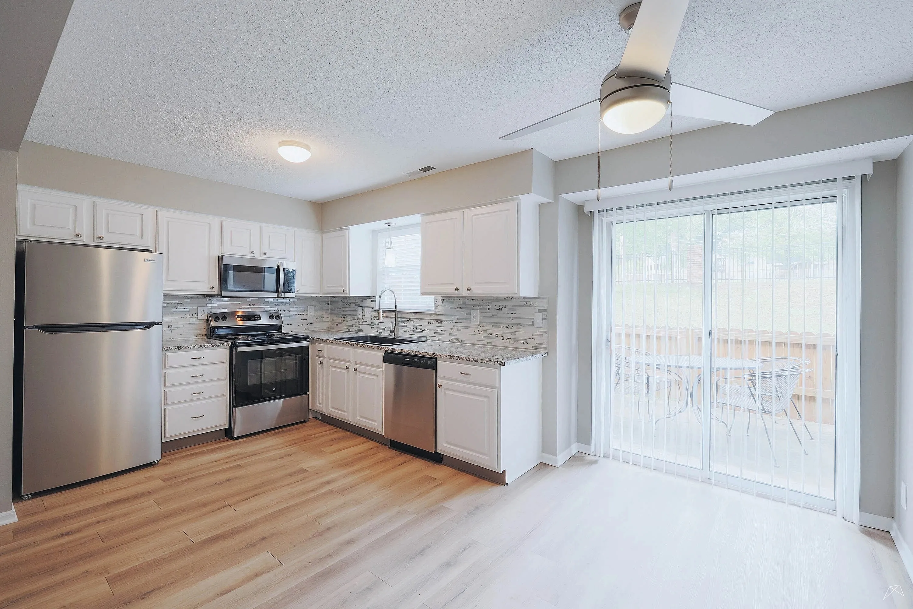 Bright, modern kitchen with stainless steel appliances, granite countertops, and stylish laminate flooring, leading to an inviting patio view.