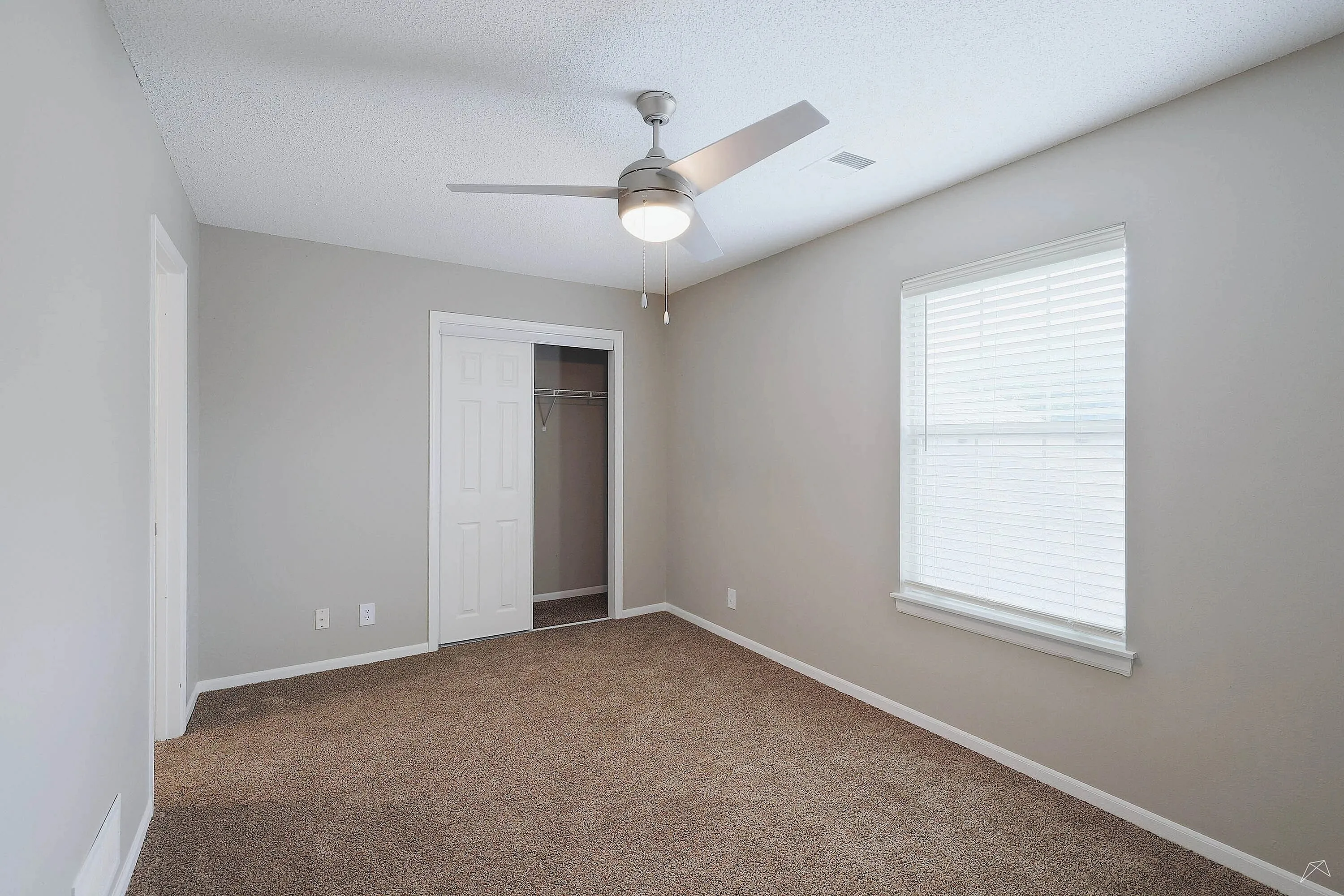 Bright and airy bedroom with plush carpeting, modern ceiling fan, and ample natural light from a large window.