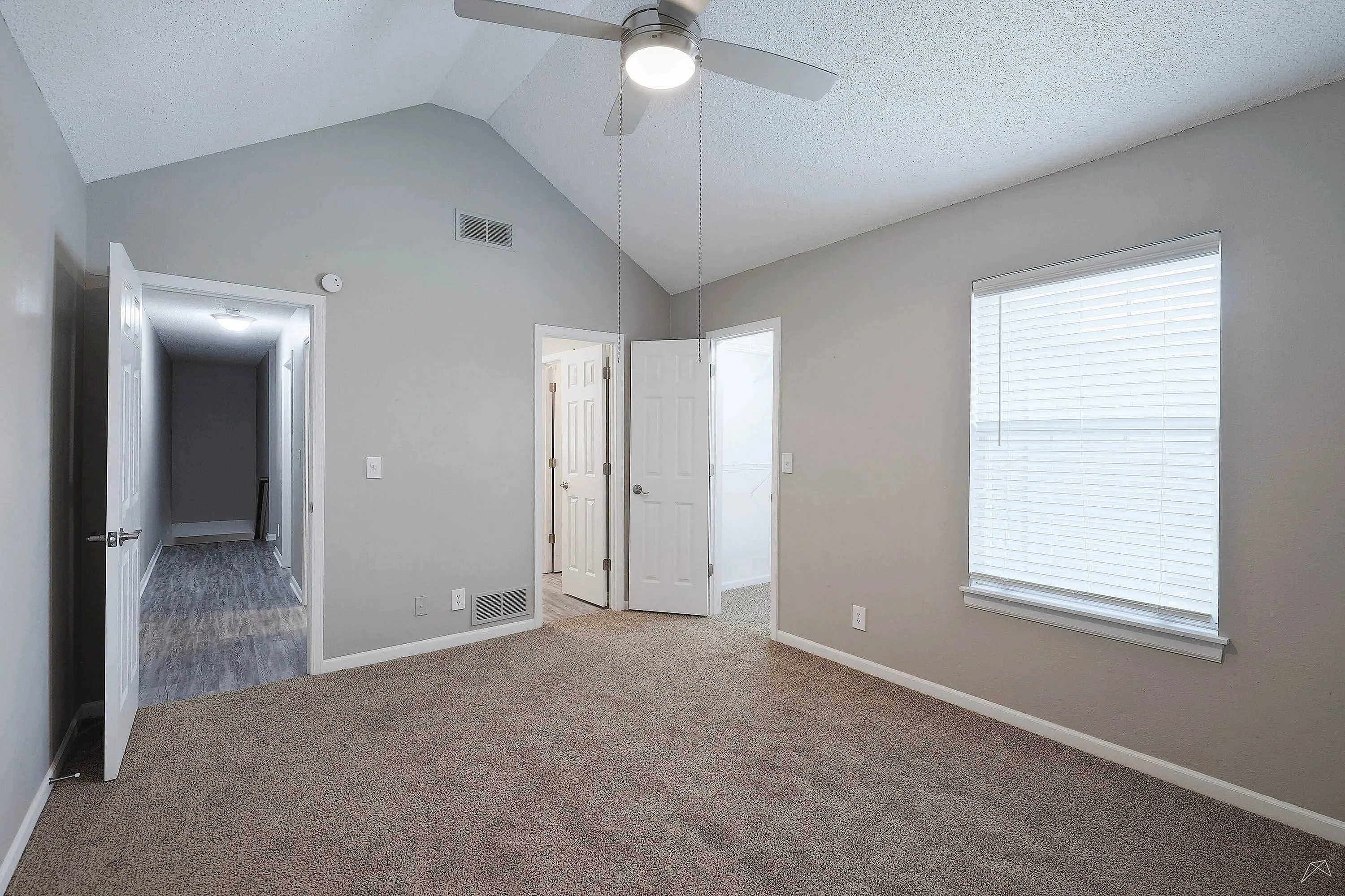 Bright and spacious bedroom with vaulted ceiling, modern fan, and plush carpet, featuring ample natural light through a large window.