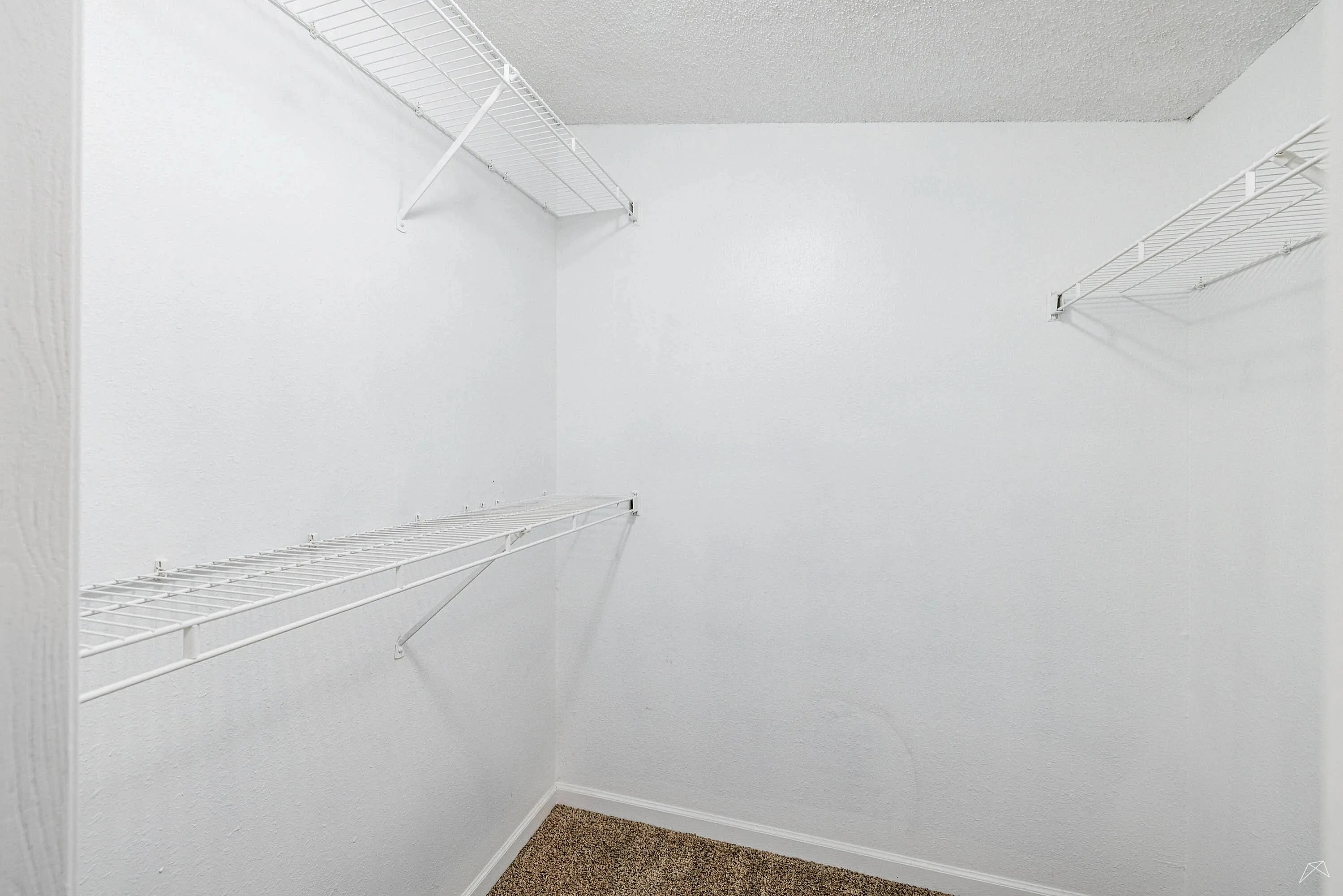 Spacious walk-in closet with sleek white shelving and plush carpeting, perfect for organized storage in a modern apartment.