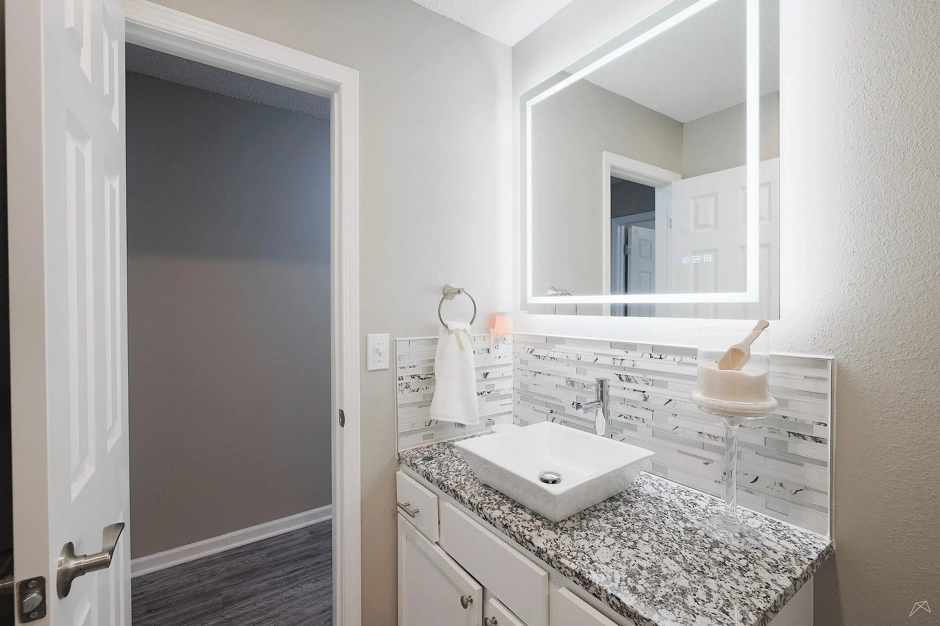 Modern bathroom with illuminated mirror, elegant granite countertop, and chic vessel sink.