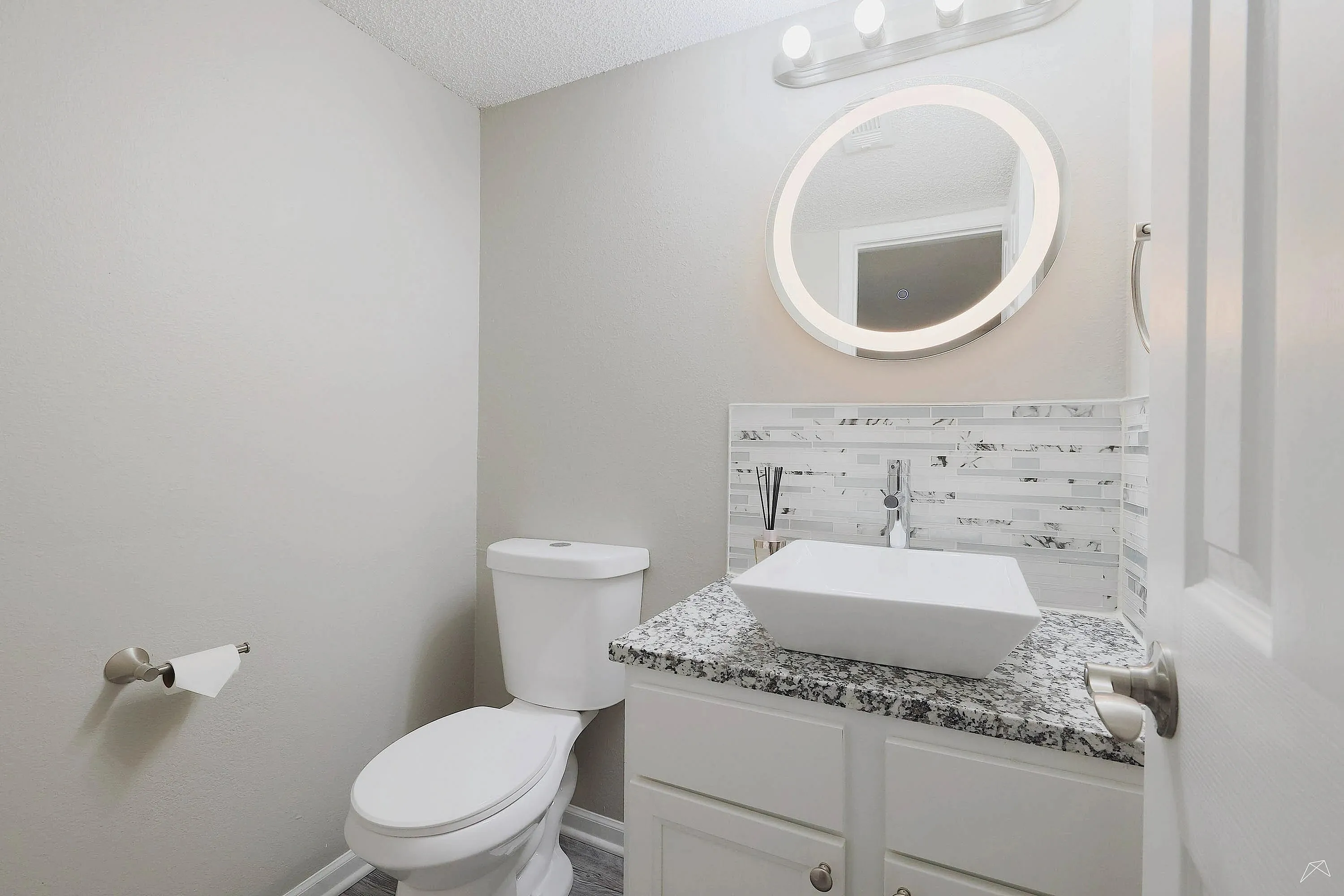 Modern bathroom featuring a circular backlit mirror, sleek vessel sink, and elegant marble countertop.