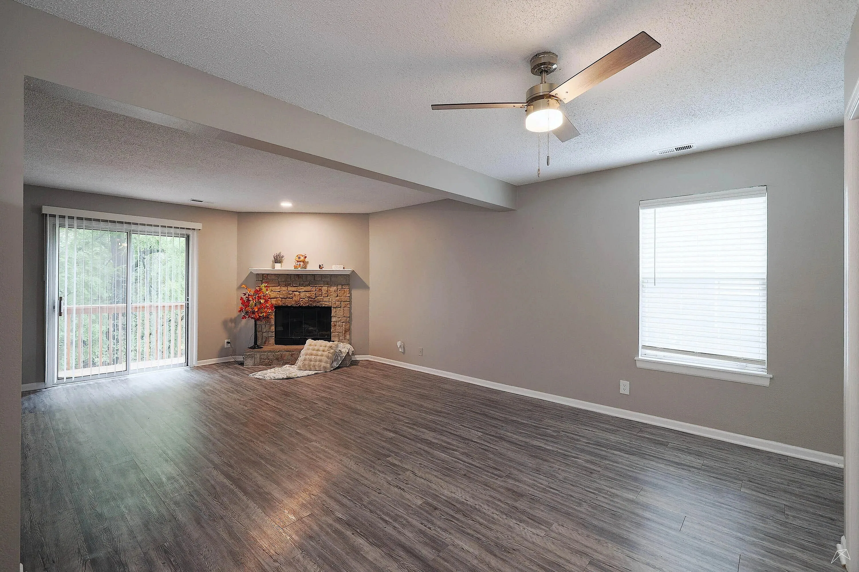 Inviting living room with modern wood flooring, cozy brick fireplace, ceiling fan, and large sliding doors to a private balcony.