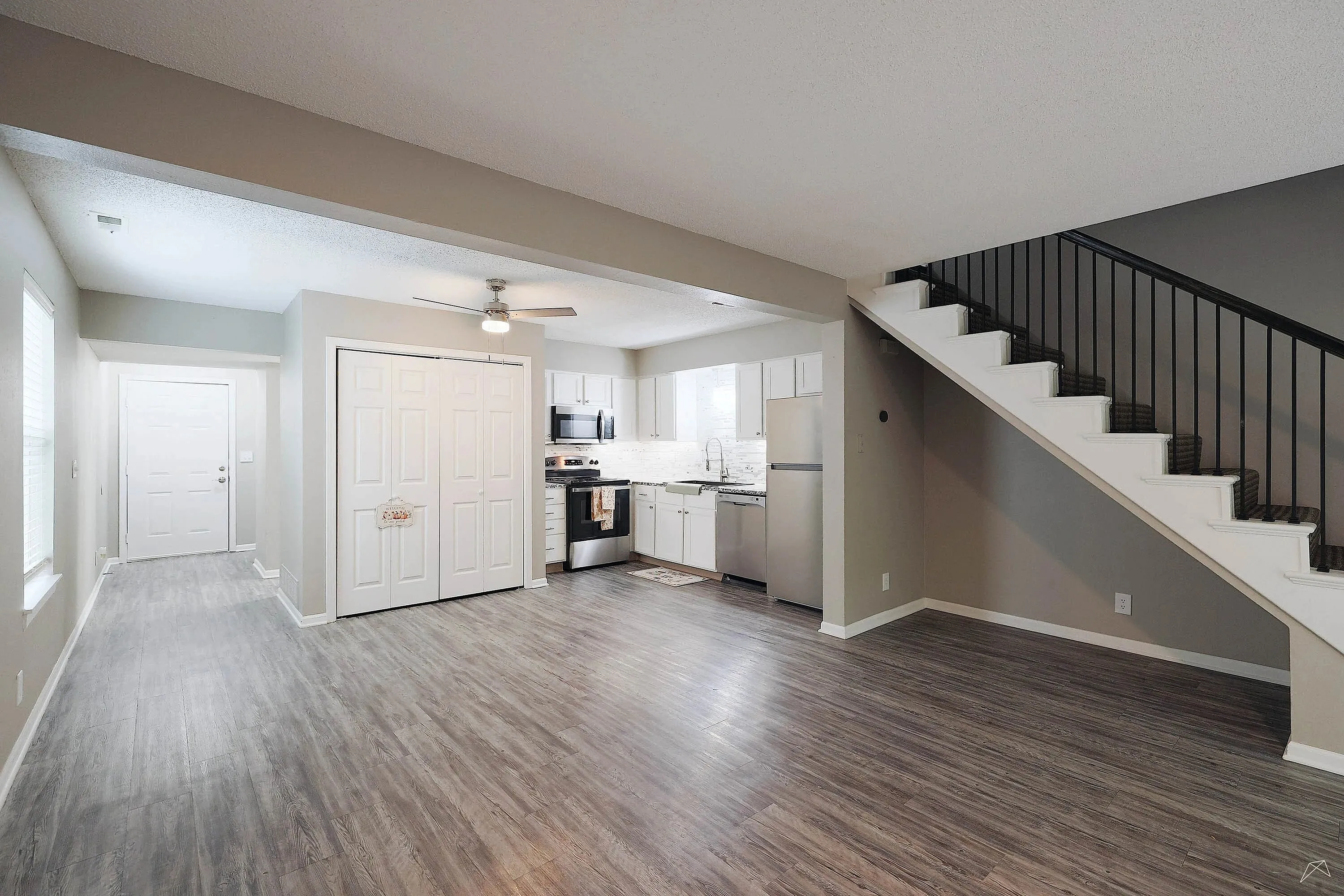 Modern open kitchen and living space with sleek stainless steel appliances and elegant staircase in a bright, airy apartment.