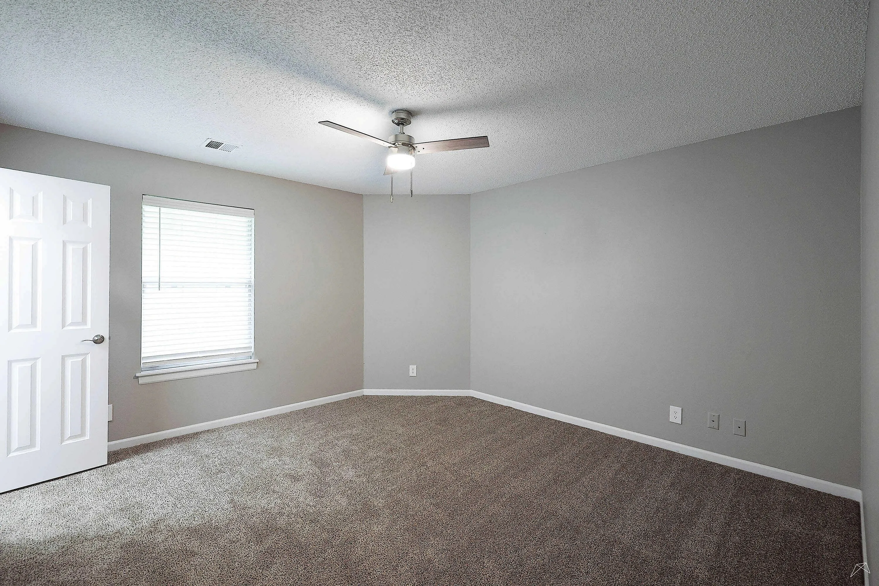 Bright and spacious empty bedroom featuring plush carpeting, a modern ceiling fan, and elegant neutral walls, perfect for personalization.