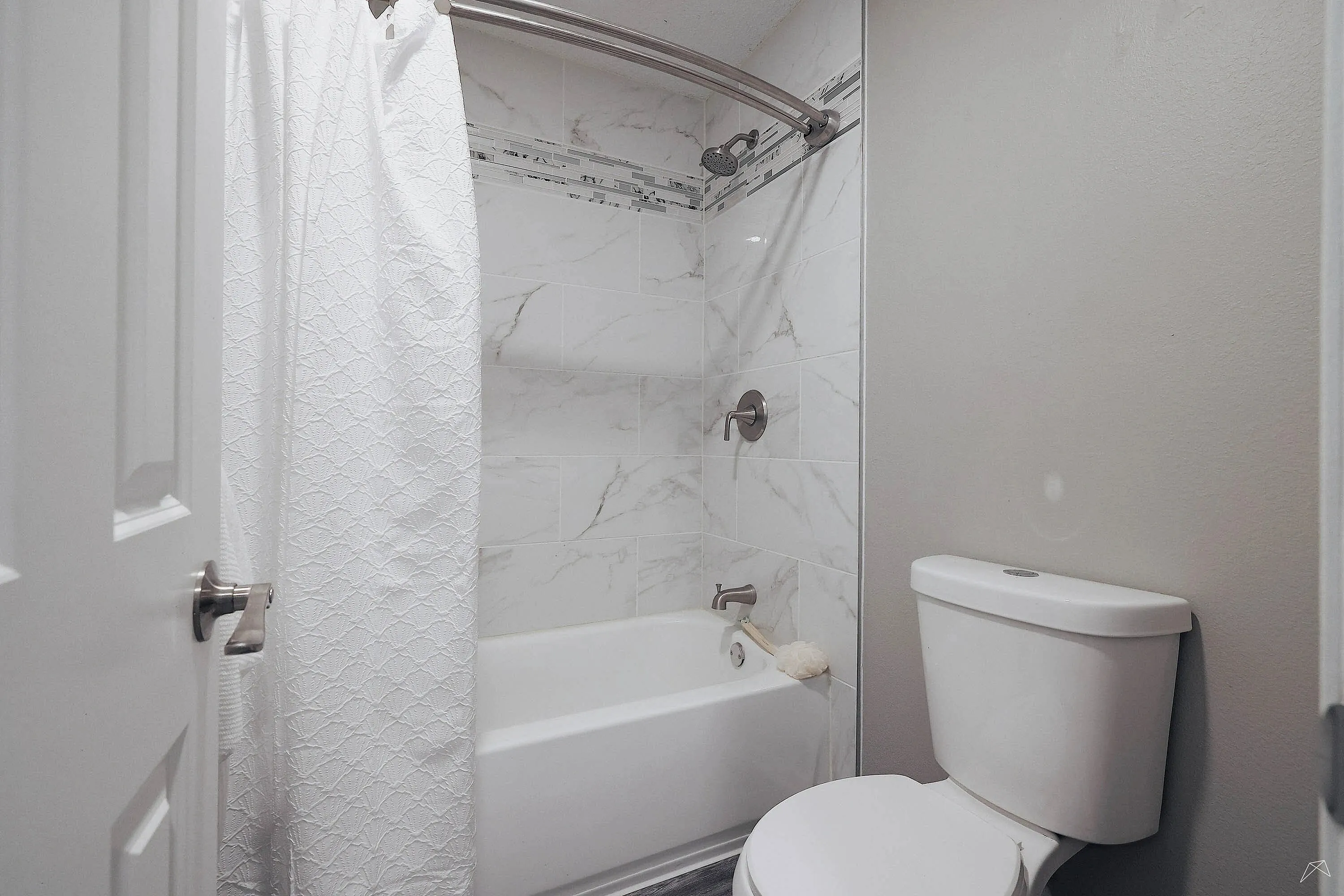 Elegant bathroom with a modern white bathtub and marble tile accents, complemented by a stylish shower curtain.