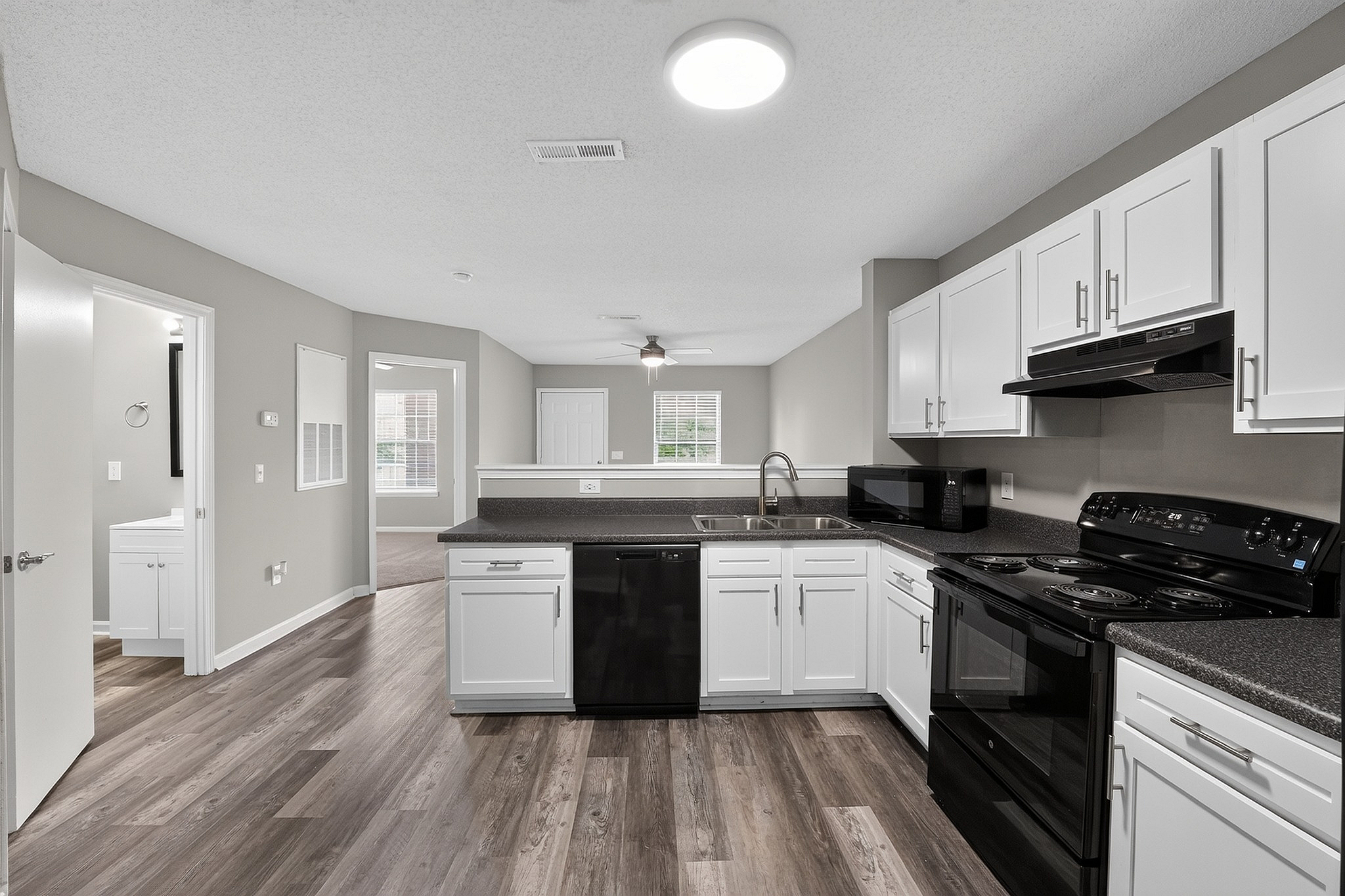 Sleek modern kitchen with stylish white cabinets, black appliances, and spacious open layout seamlessly connecting to the well-lit living area.