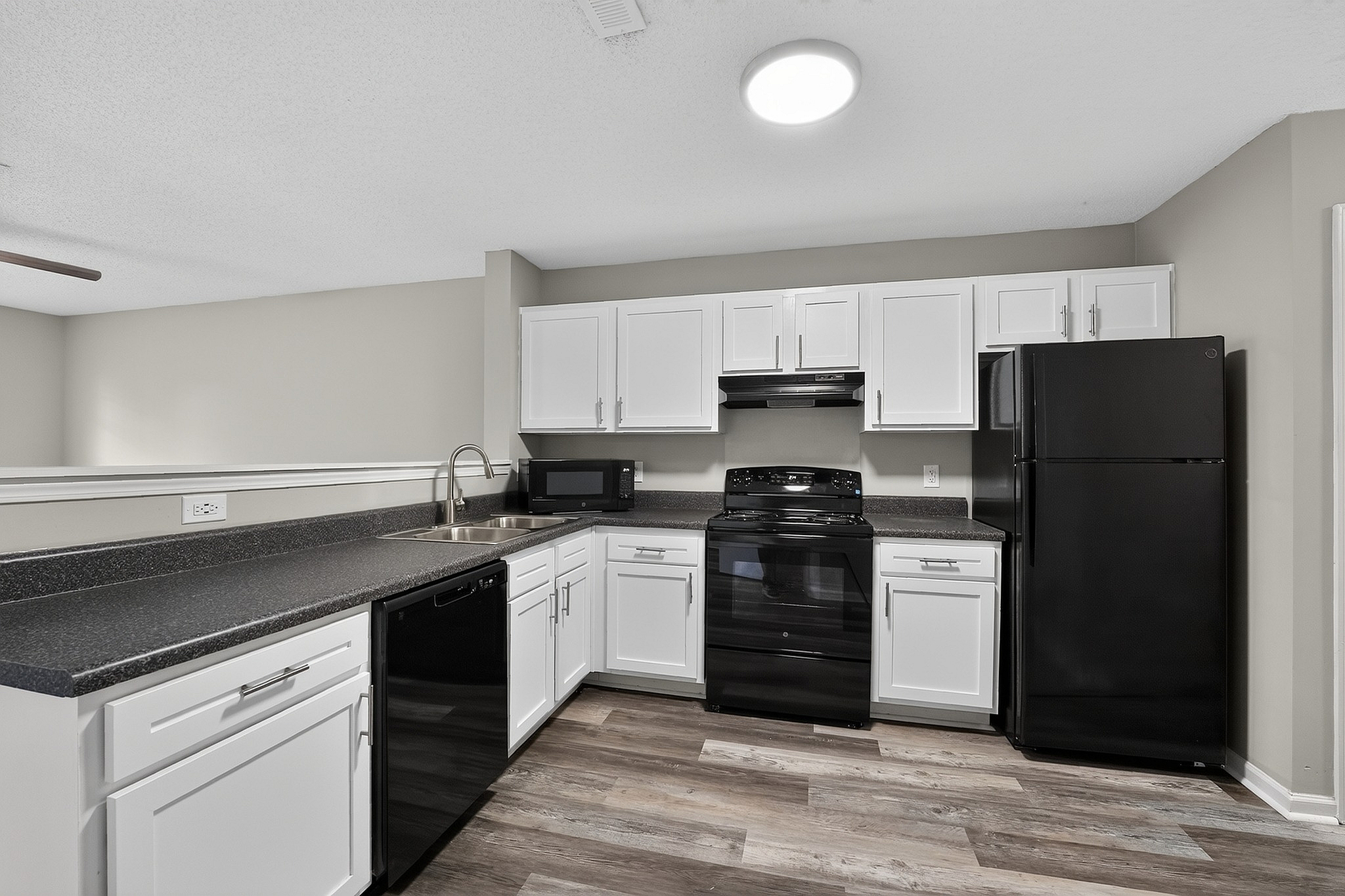 Modern kitchen with sleek black appliances, white cabinetry, and elegant laminate flooring.