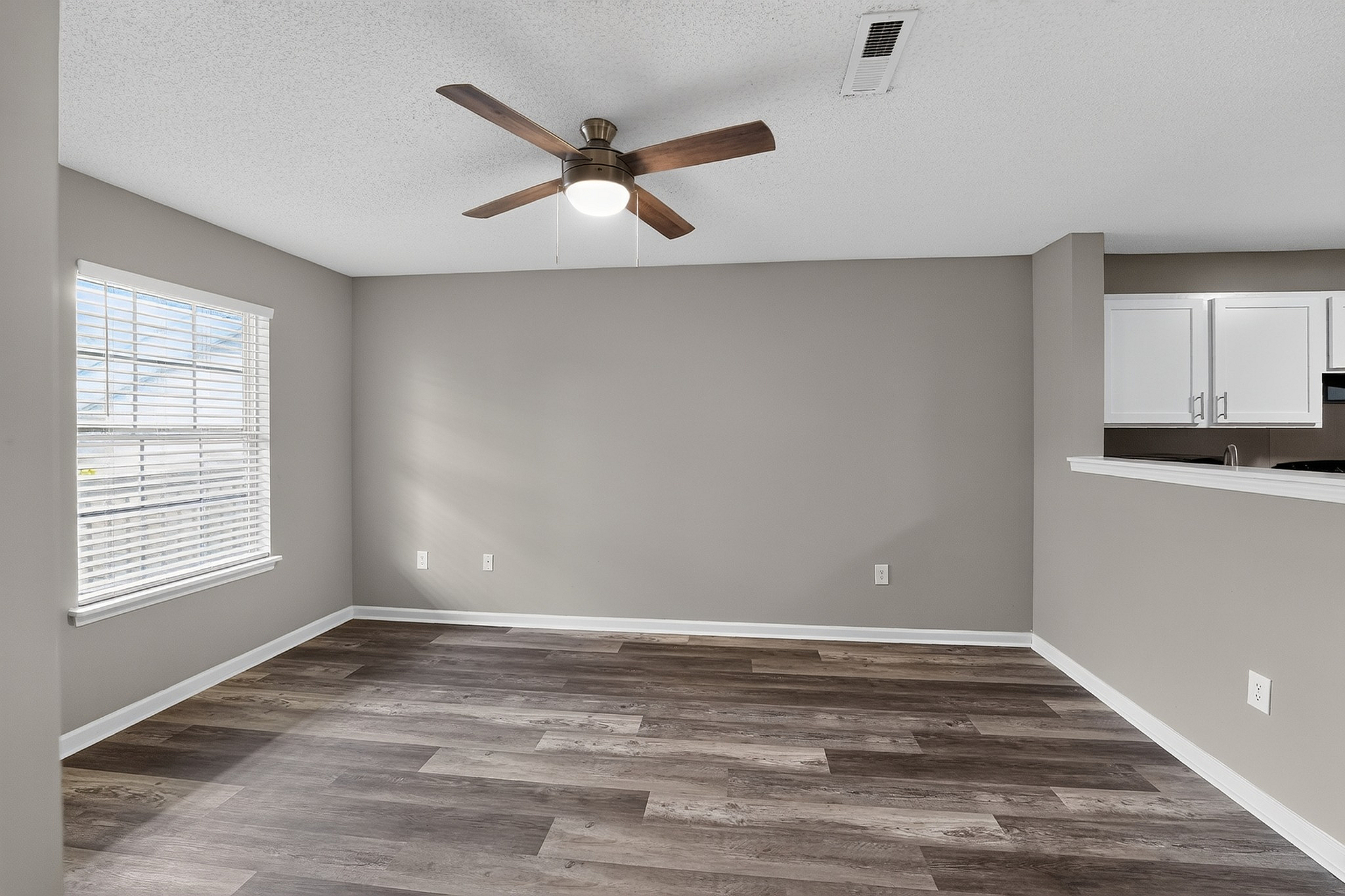 Bright and modern living area with sleek flooring, large window, and open access to a contemporary white kitchen.