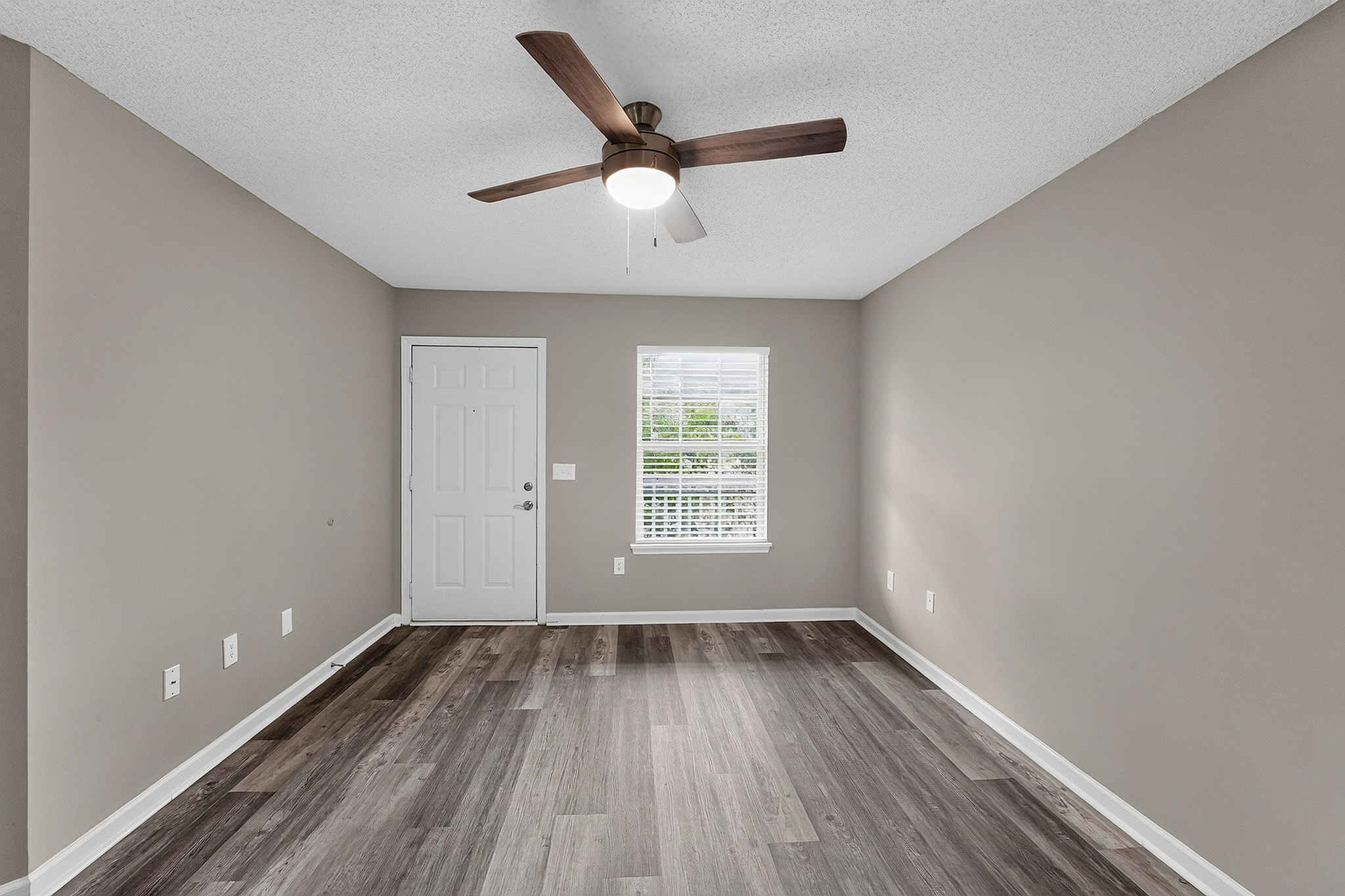 Bright, modern living space featuring sleek wood flooring, fresh neutral walls, and a contemporary ceiling fan.