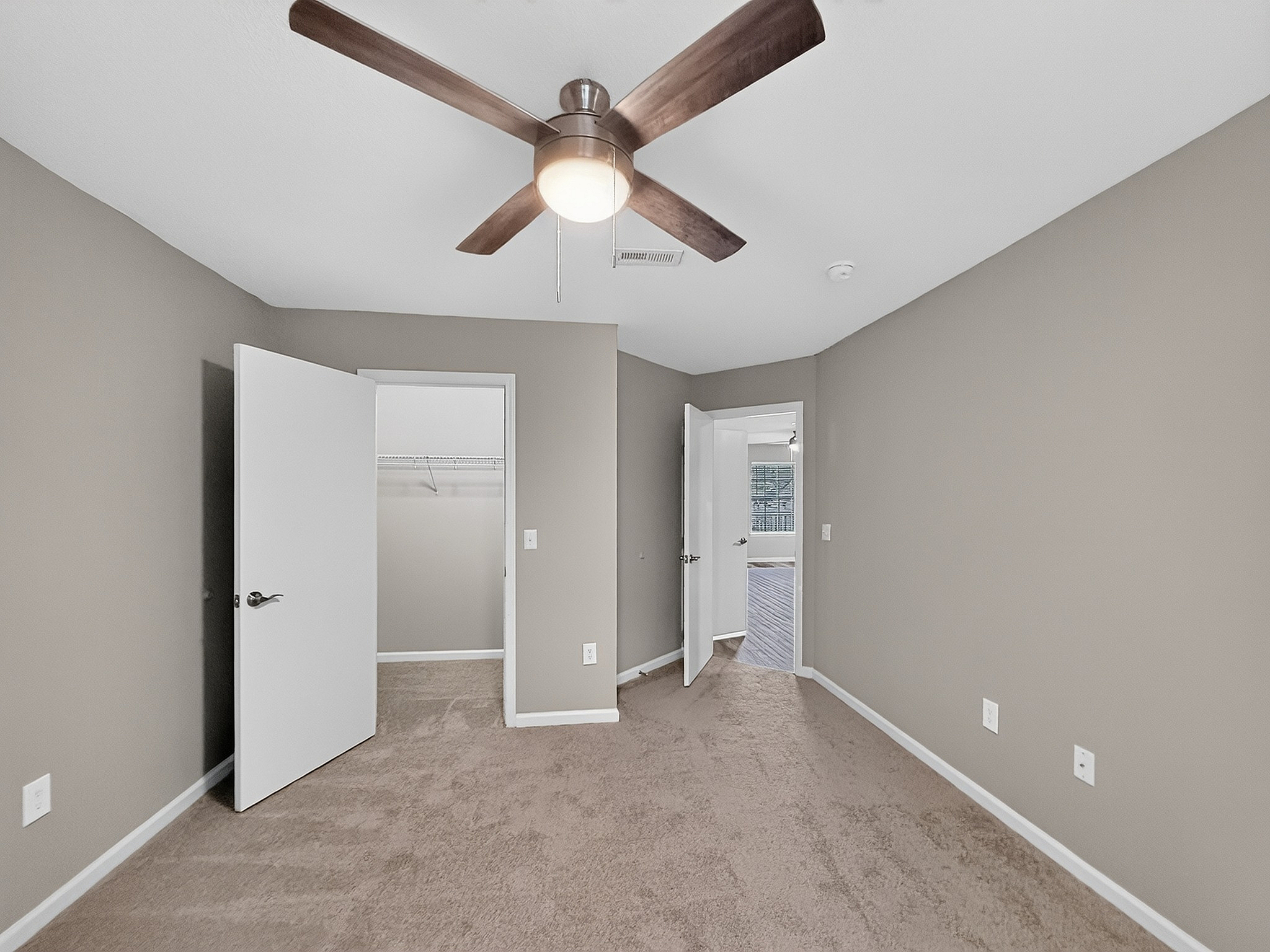 Inviting bedroom with cozy carpet, neutral walls, and a modern ceiling fan, leading to a spacious walk-in closet.