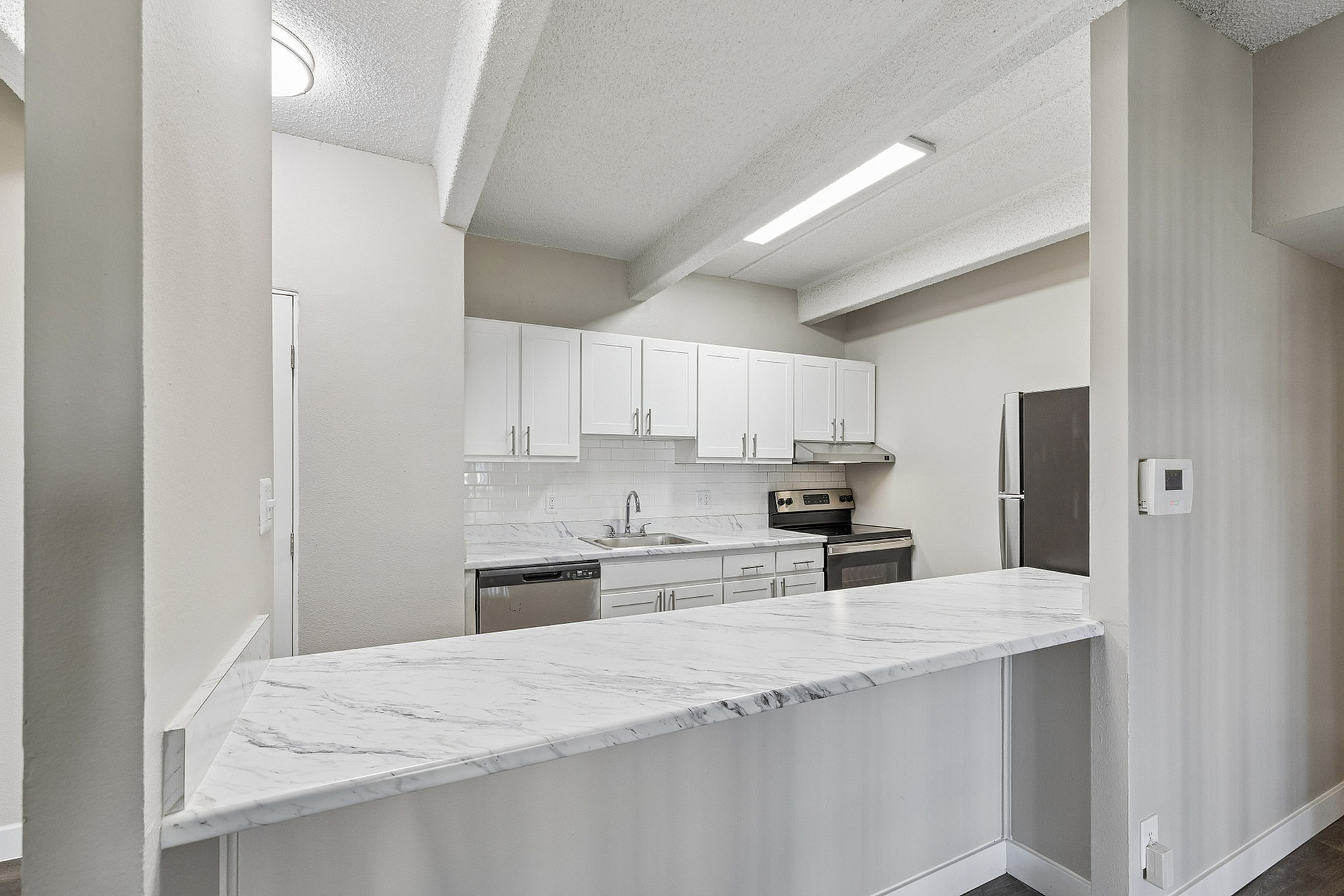 Modern kitchen with sleek white cabinetry, marble countertops, and stainless steel appliances, exuding contemporary elegance.
