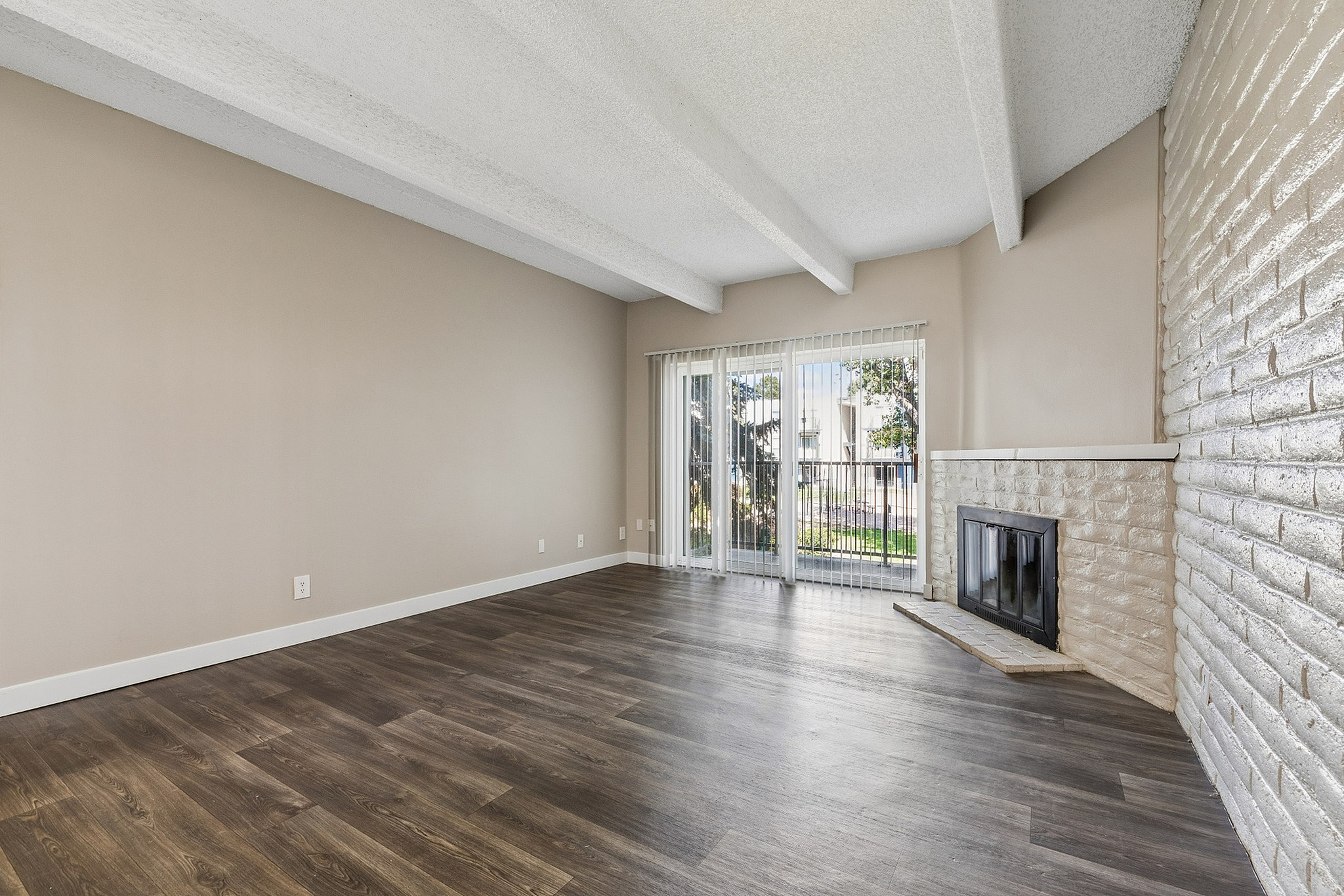 Inviting living room with sleek hardwood floors, stylish white brick fireplace, and expansive sliding glass doors leading to a beautiful garden view.