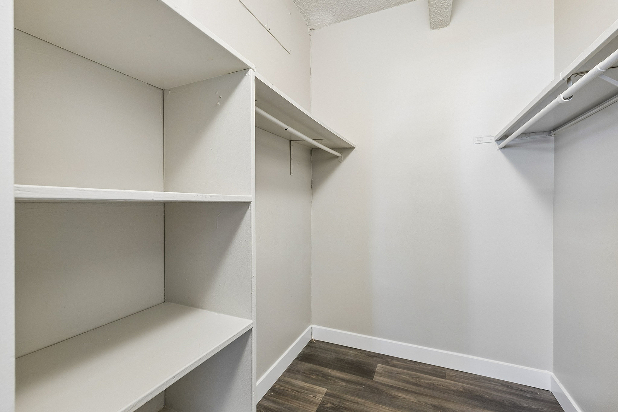 Spacious walk-in closet with sleek white shelving and modern wooden flooring, offering ample storage space.