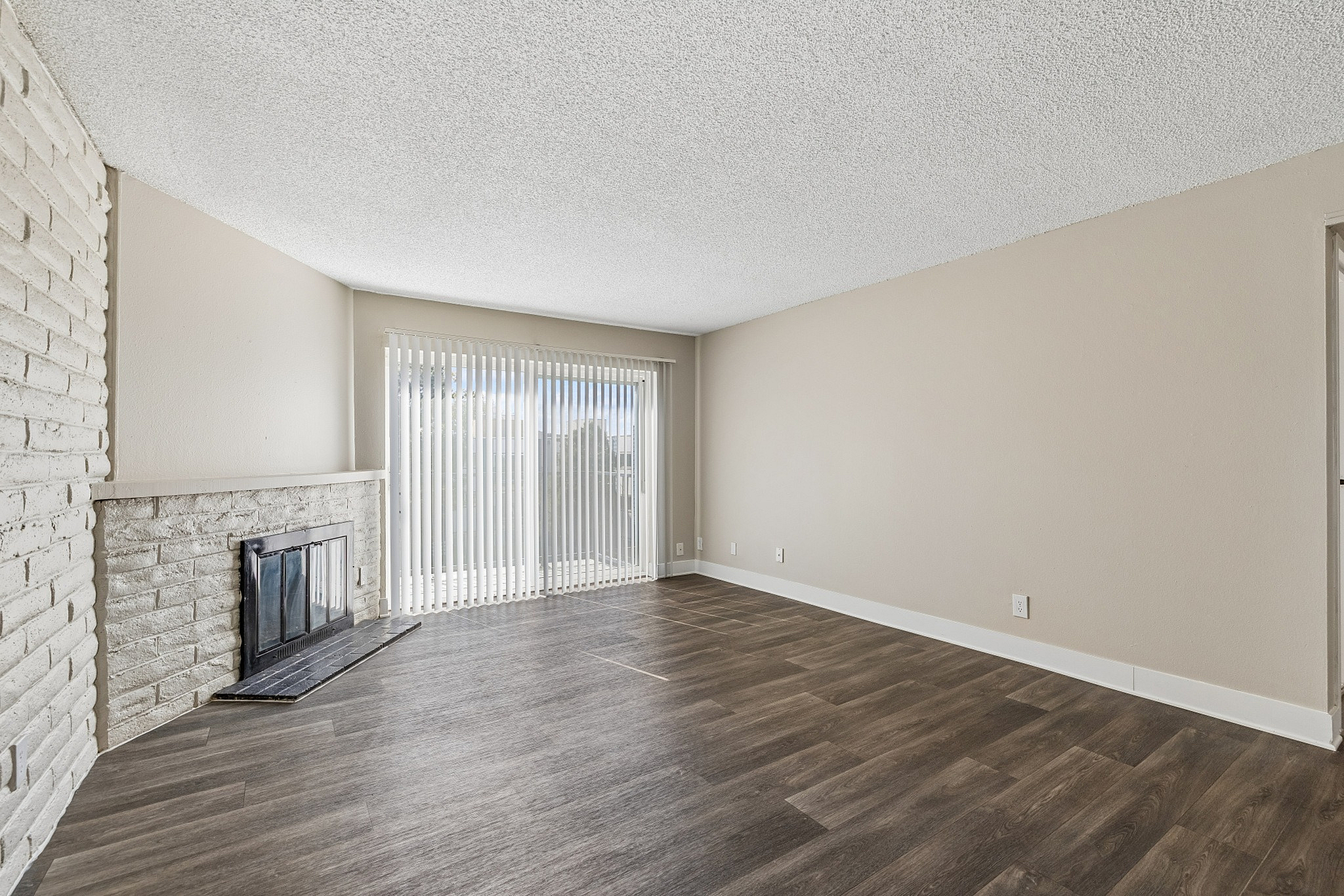 Spacious living room featuring elegant wood flooring, a cozy fireplace, and large sliding glass doors with vertical blinds.
