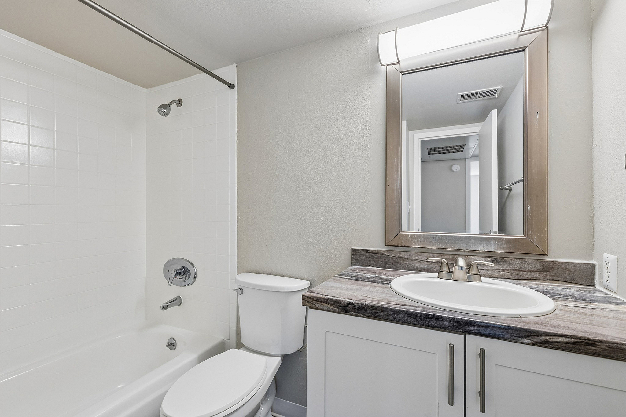 Modern bathroom with elegant design featuring a sleek vanity, well-lit mirror, and pristine bathtub.