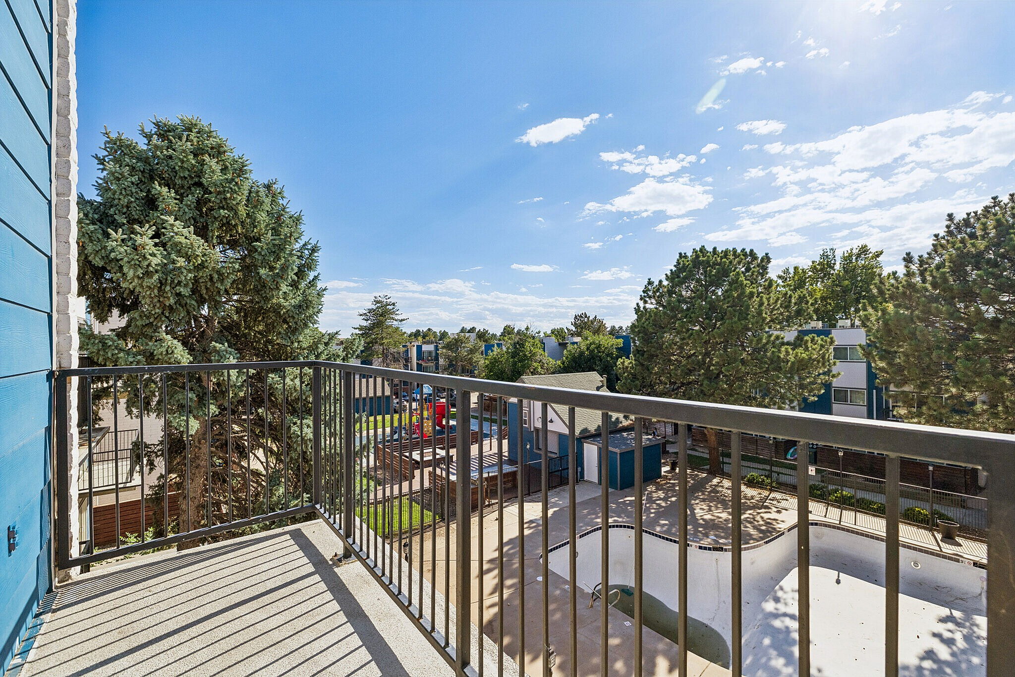 Inviting balcony with sunlit views of lush trees and a serene community pool, ideal for relaxation and outdoor enjoyment.