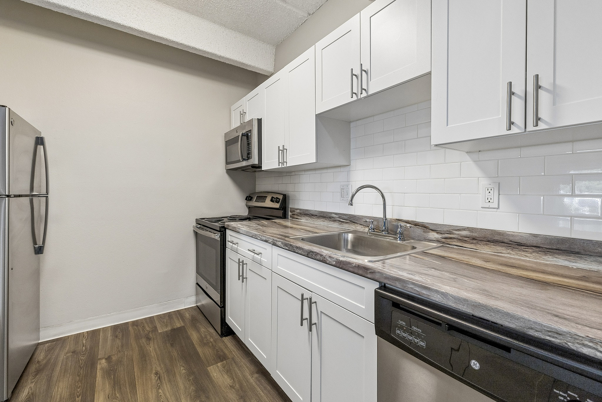 Modern kitchen with stainless steel appliances, elegant white cabinetry, and stylish wood flooring.
