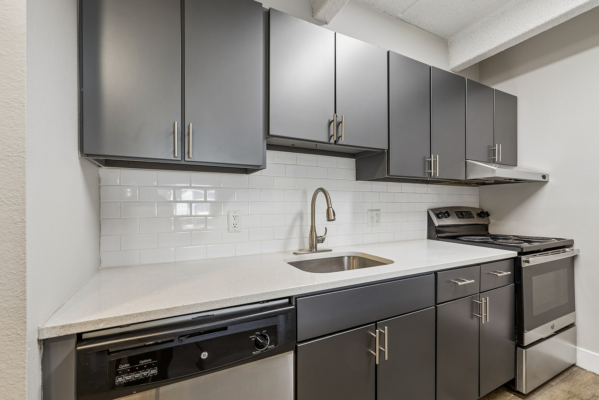 Modern kitchen with sleek gray cabinets, stainless steel appliances, and elegant white subway tile backsplash.