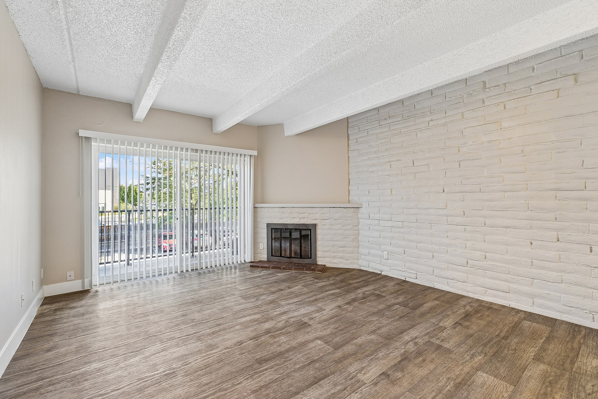 Bright living room with large windows, wooden floors, and a cozy brick fireplace, perfect for relaxation.