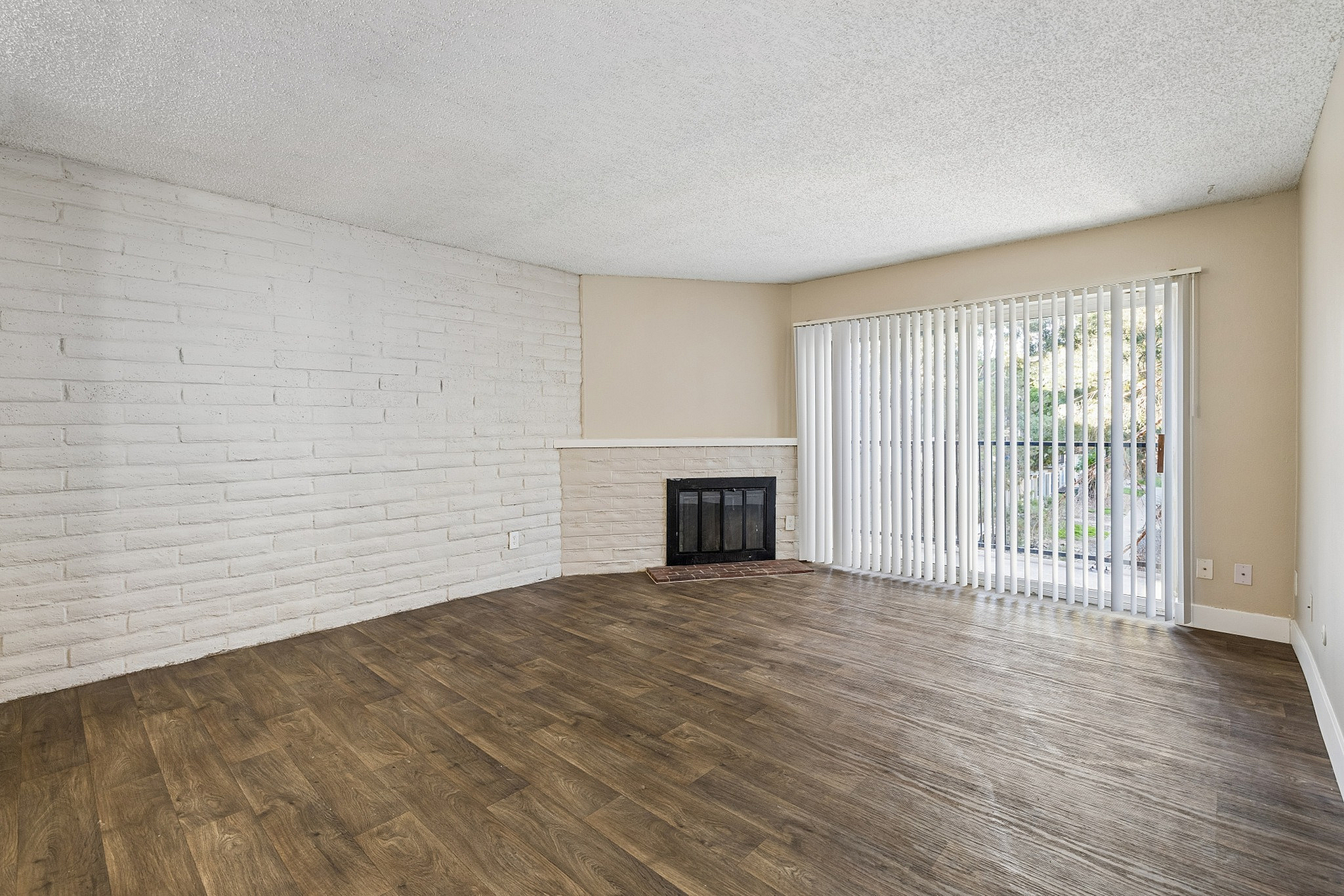 Inviting living room with elegant wood flooring, a charming brick fireplace, and expansive glass doors leading to a serene outdoor view.