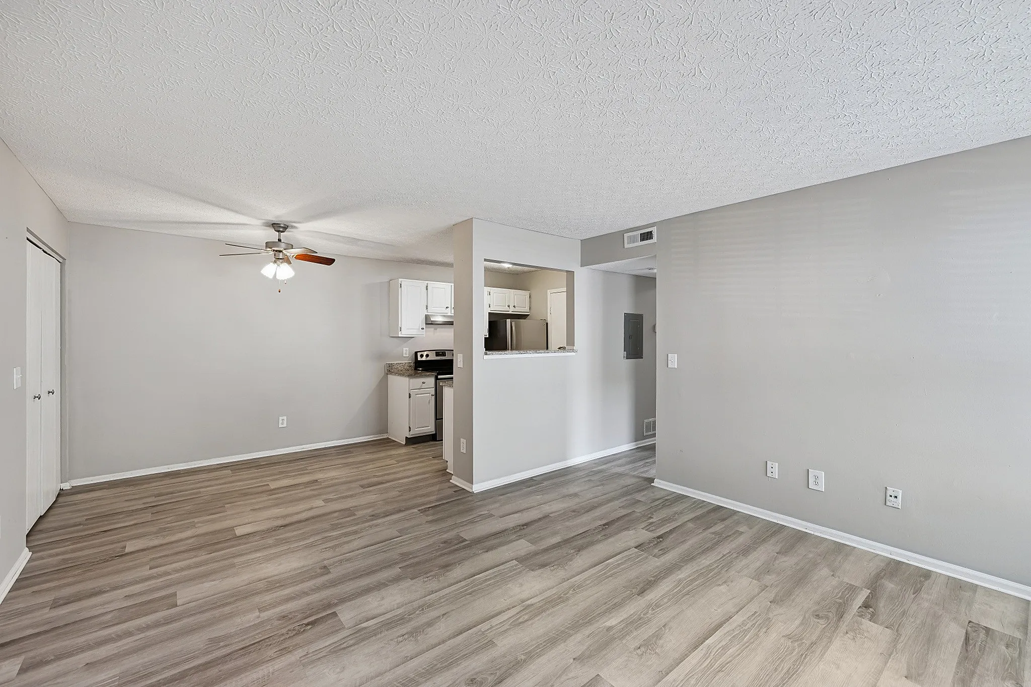 Bright and open living space with modern hardwood floors, ceiling fan, and a cozy kitchen view in a contemporary apartment.