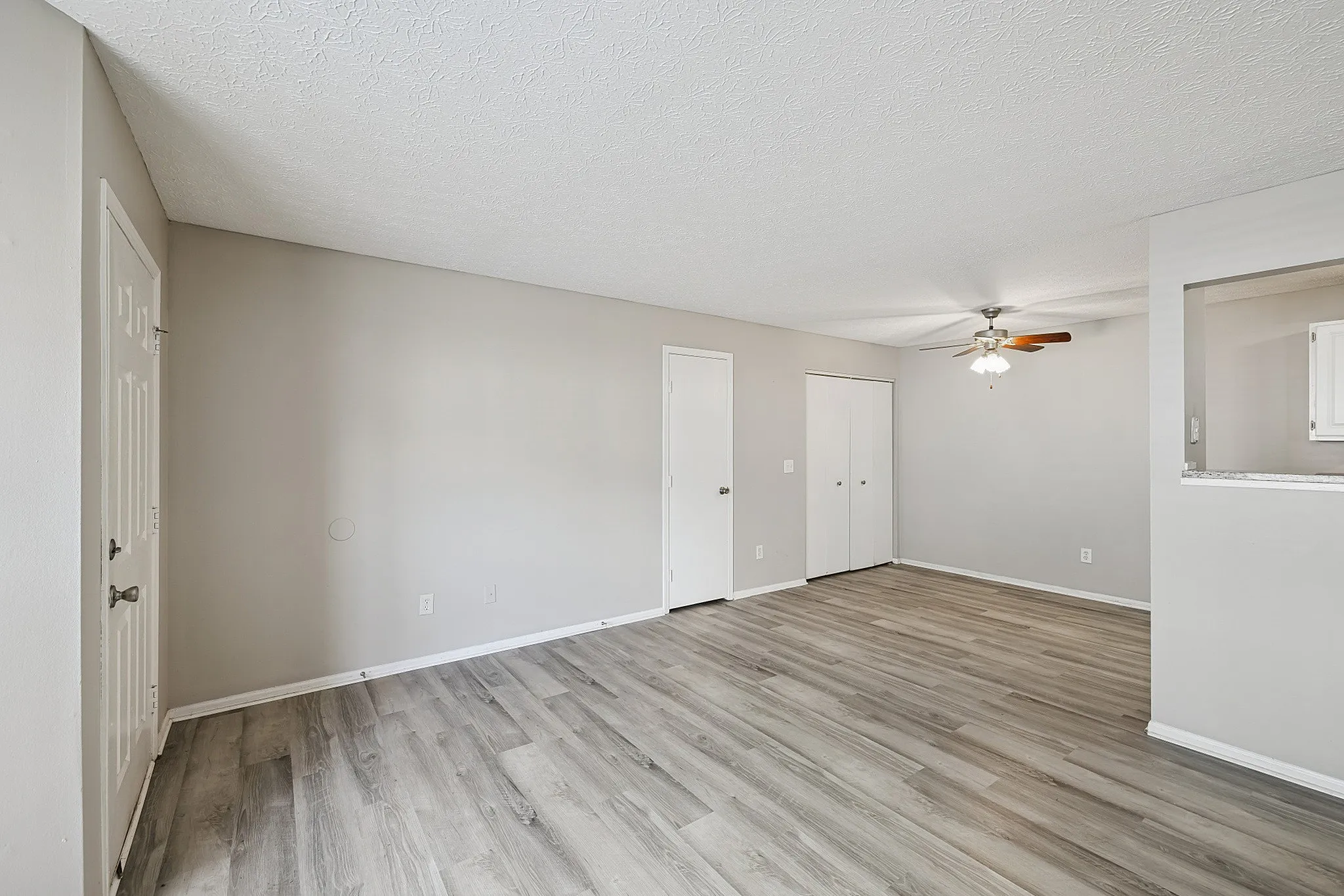 Spacious empty apartment room with modern gray wood flooring, neutral walls, and ceiling fan, ready for personal styling.