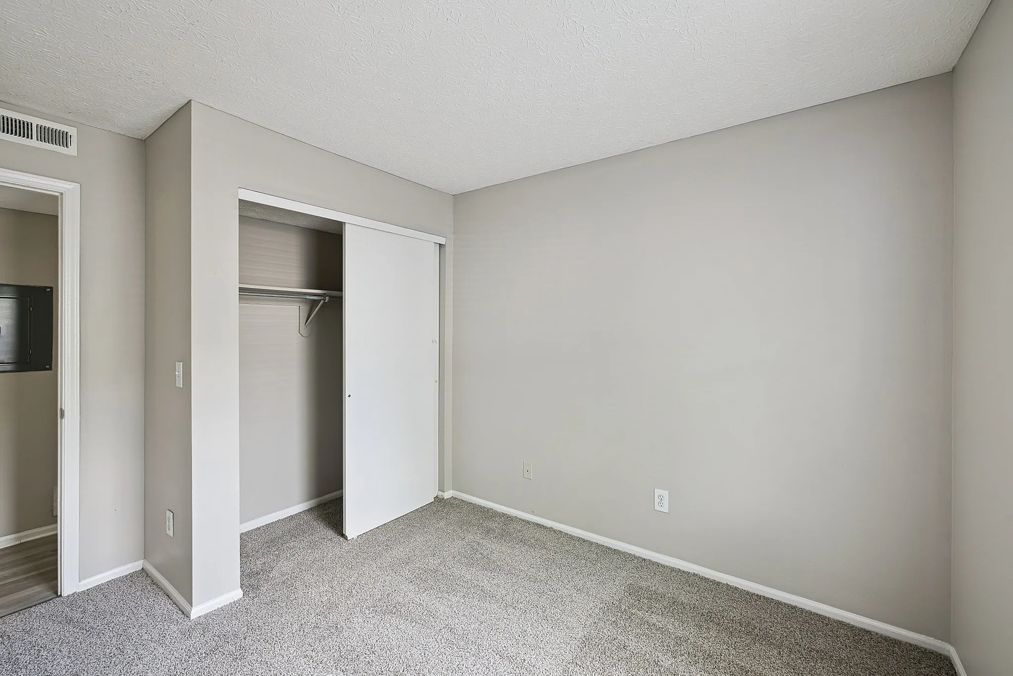Bright and airy bedroom with neutral walls, plush carpet, and a spacious closet for modern living.