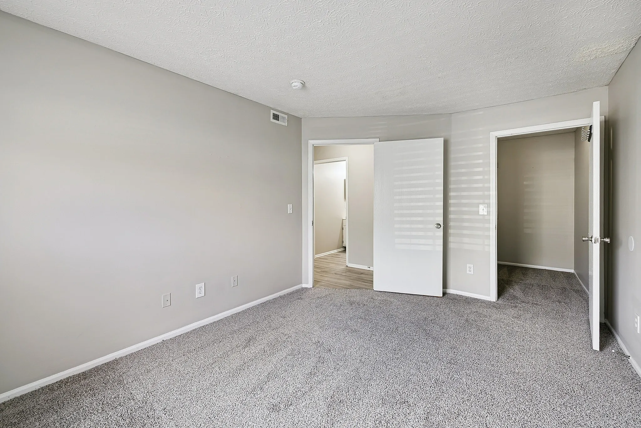 Inviting bedroom with plush carpeting and elegant neutral walls, featuring an open doorway to an additional space for versatile living.