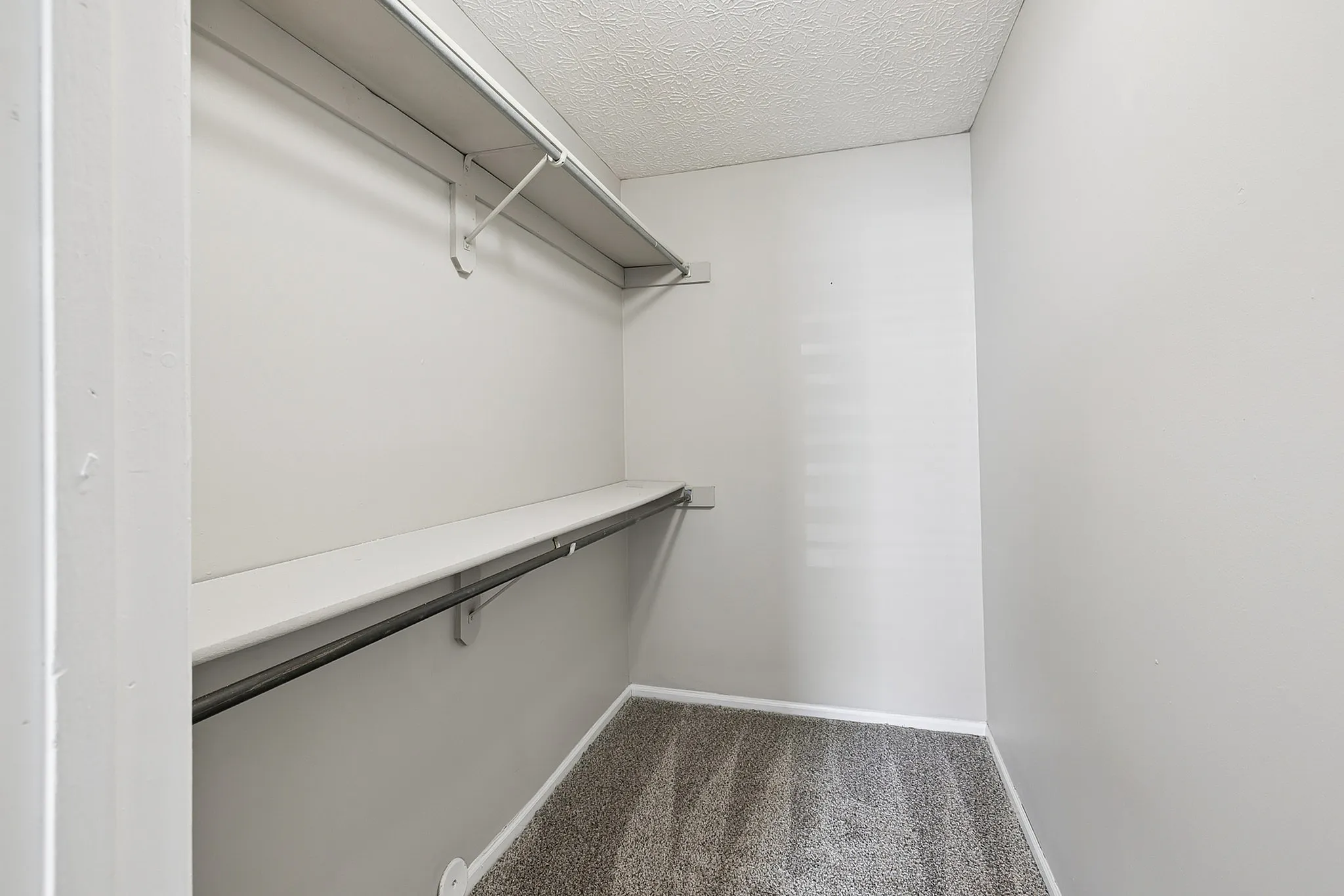 Bright and spacious walk-in closet with built-in shelving and modern textured ceiling, perfect for ample storage.
