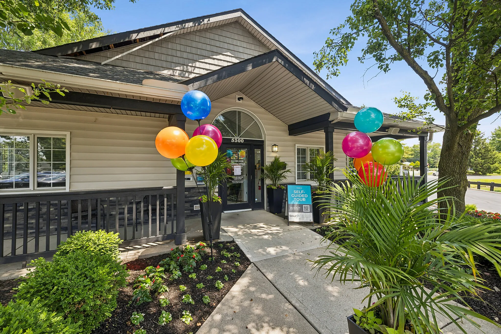 Inviting apartment entrance with vibrant balloons, lush greenery, and a self-guided tour sign, creating a welcoming atmosphere.