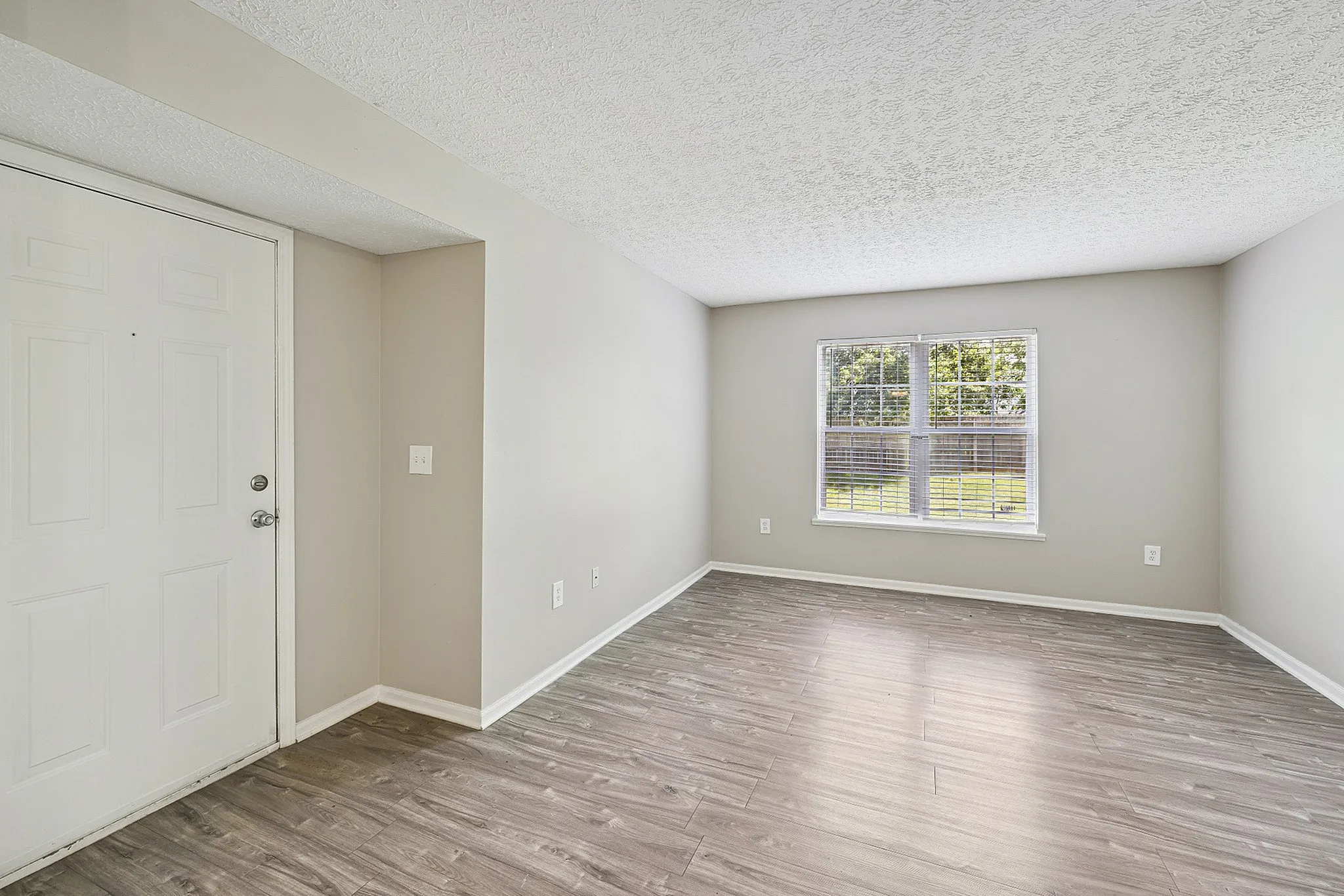 Bright and spacious apartment entryway featuring sleek wood flooring and a large window inviting natural light.
