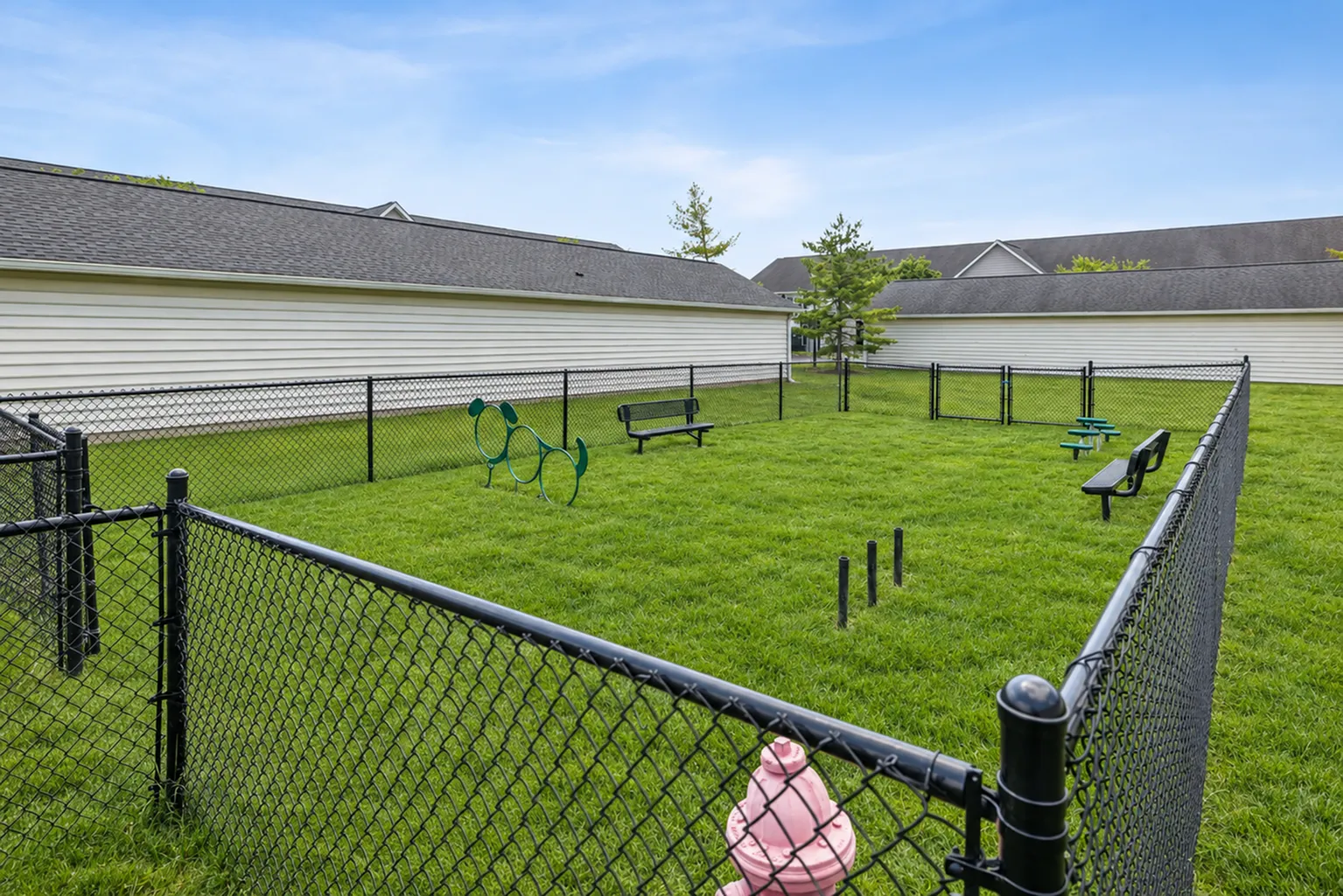 Charming apartment community featuring a fenced dog park with agility equipment and benches, perfect for pet owners.