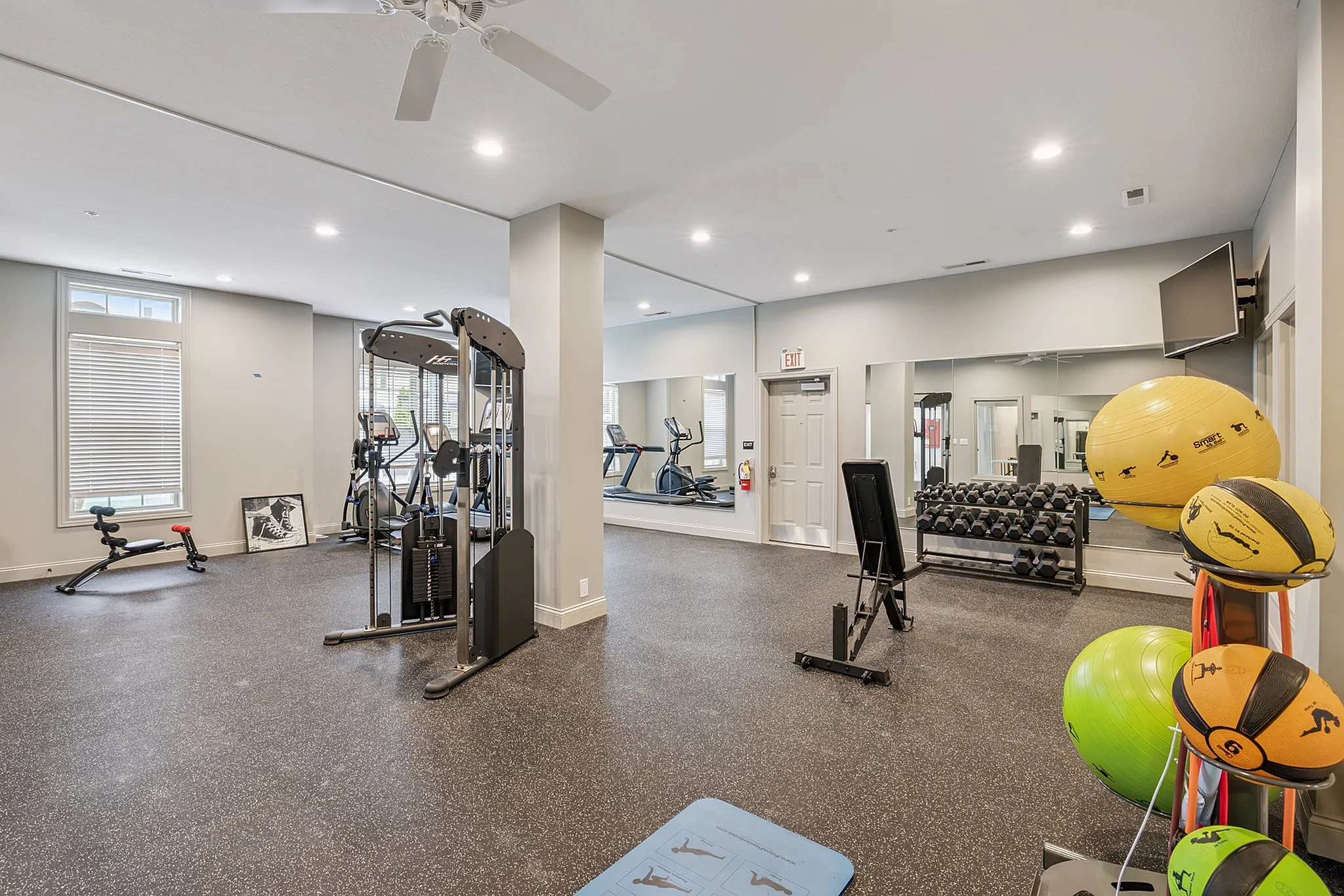 Bright and spacious apartment gym with modern exercise equipment, including weights, a treadmill, and yoga balls, inviting fitness enthusiasts.