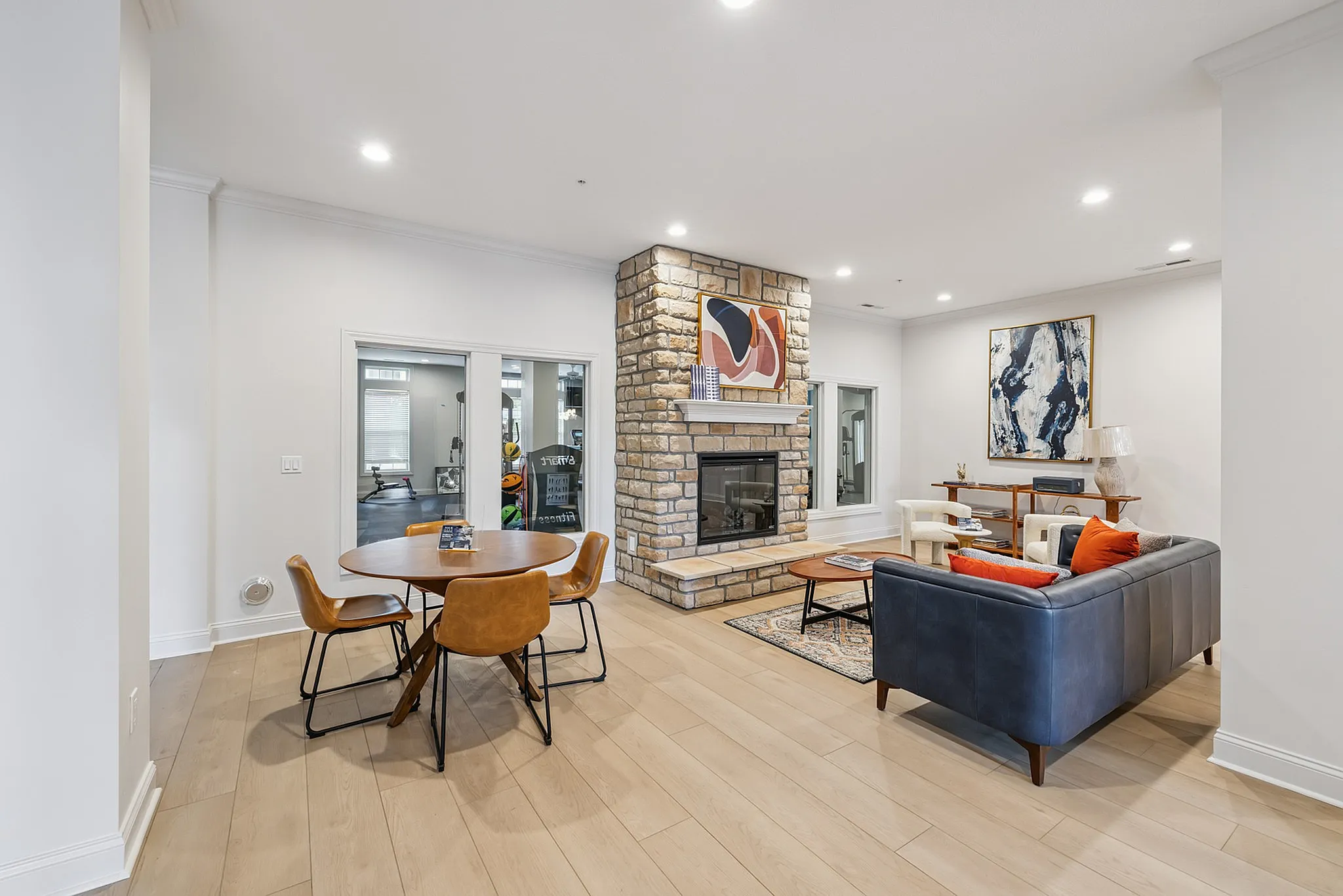Sophisticated living room with sleek hardwood floors, a cozy leather sofa, modern stone fireplace, and stylish dining area.