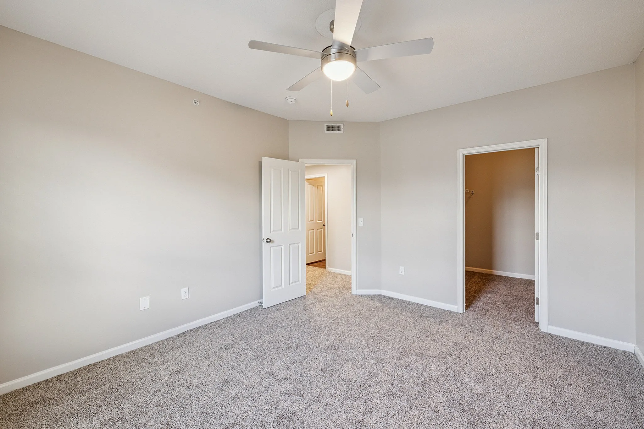 Bright and spacious bedroom with plush carpeting, ceiling fan, and walk-in closet in a modern apartment.