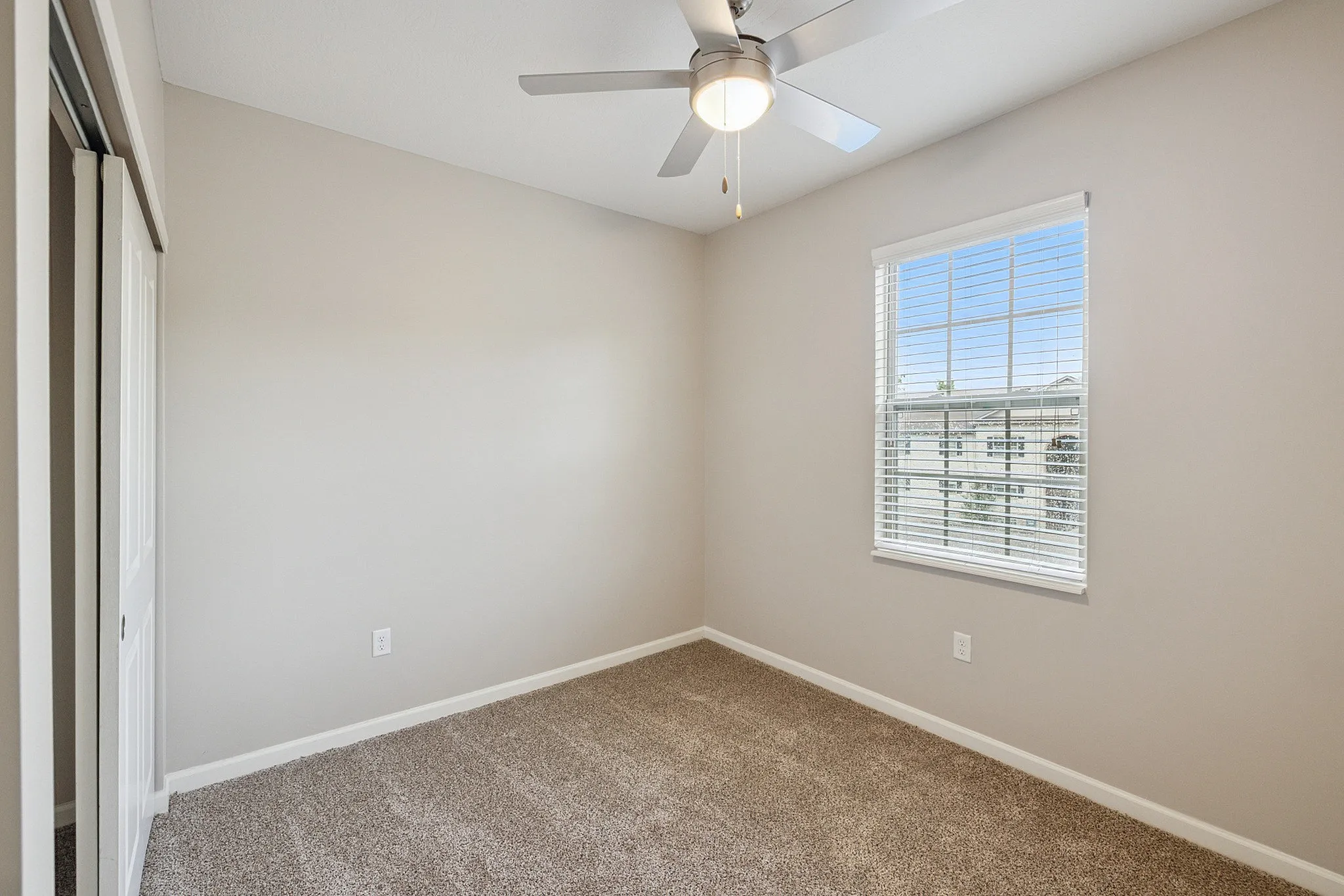Bright, cozy bedroom with plush carpet, a light-filled window, and a modern ceiling fan.