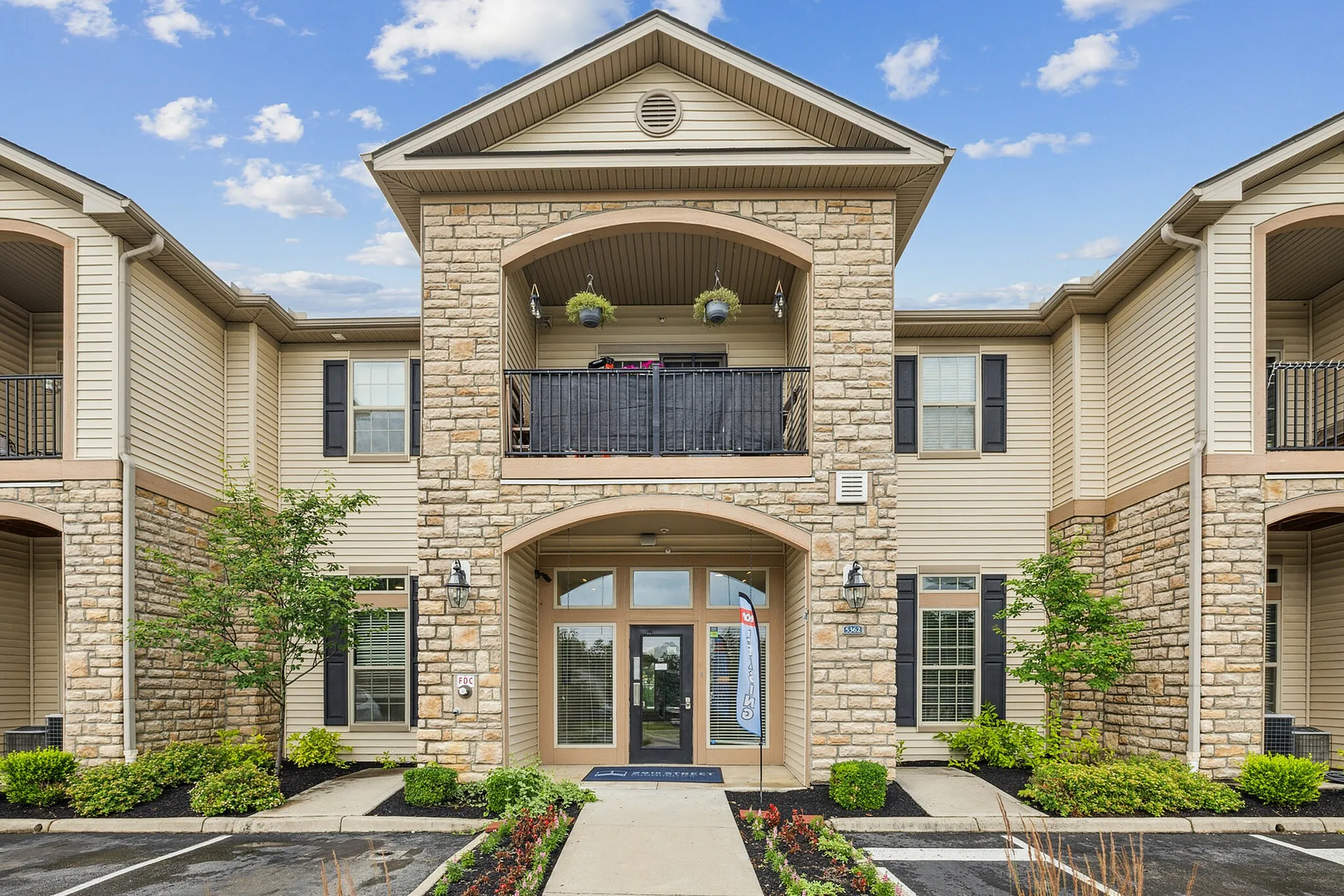 Elegant apartment building with stone façade, stylish balconies, and lush landscaping under a vibrant blue sky.