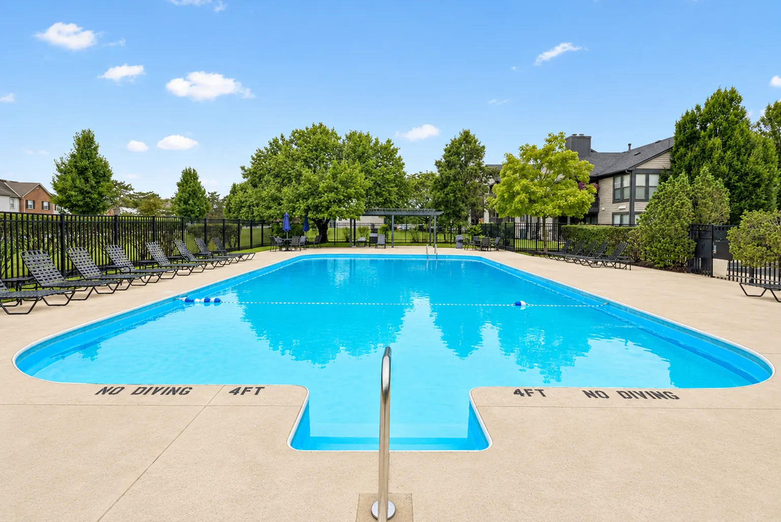 Inviting outdoor swimming pool surrounded by lush trees and sun loungers, perfect for relaxing and enjoying sunny days.