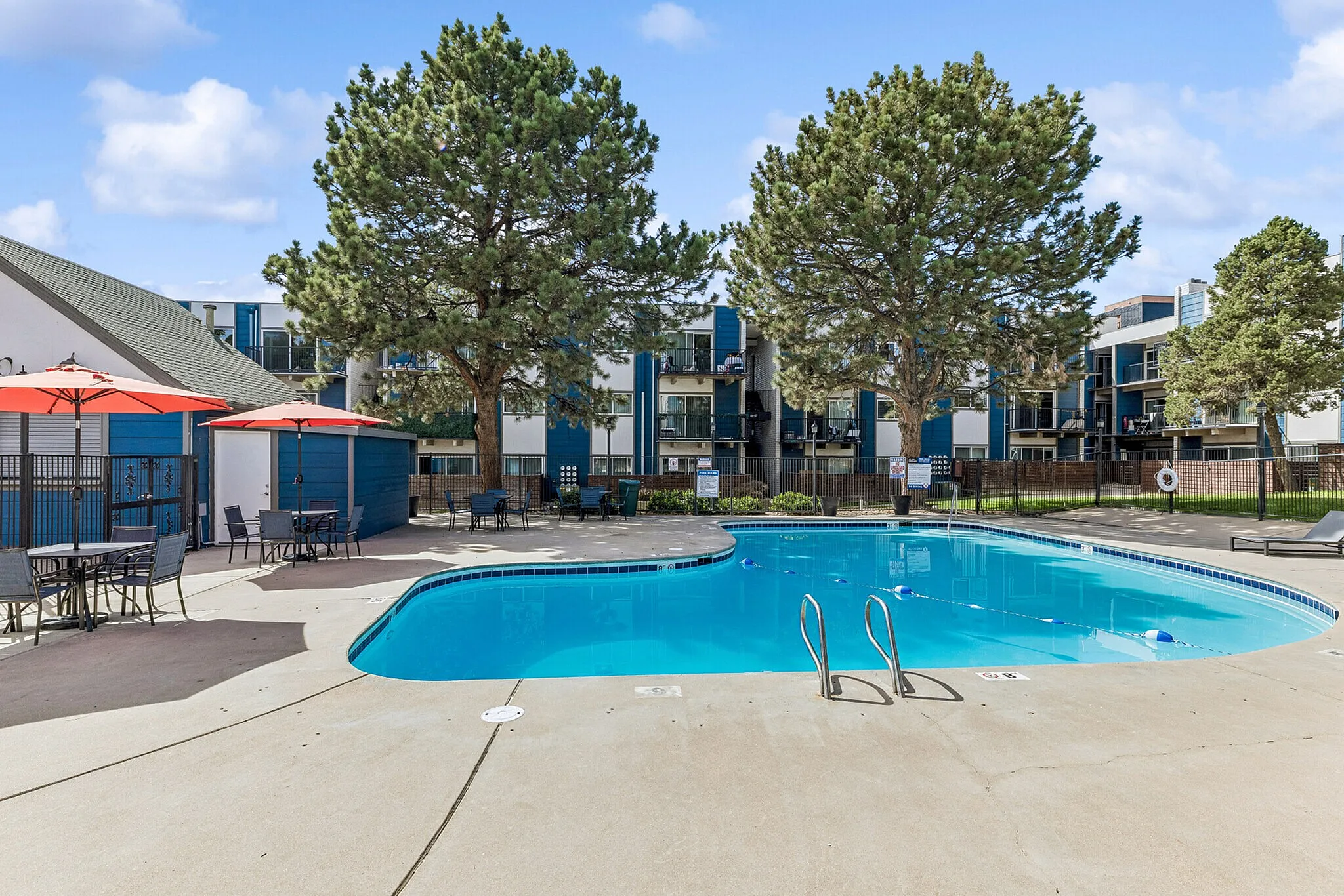 Inviting outdoor swimming pool area with vibrant red umbrellas and lush trees, perfect for relaxation in a modern apartment complex.