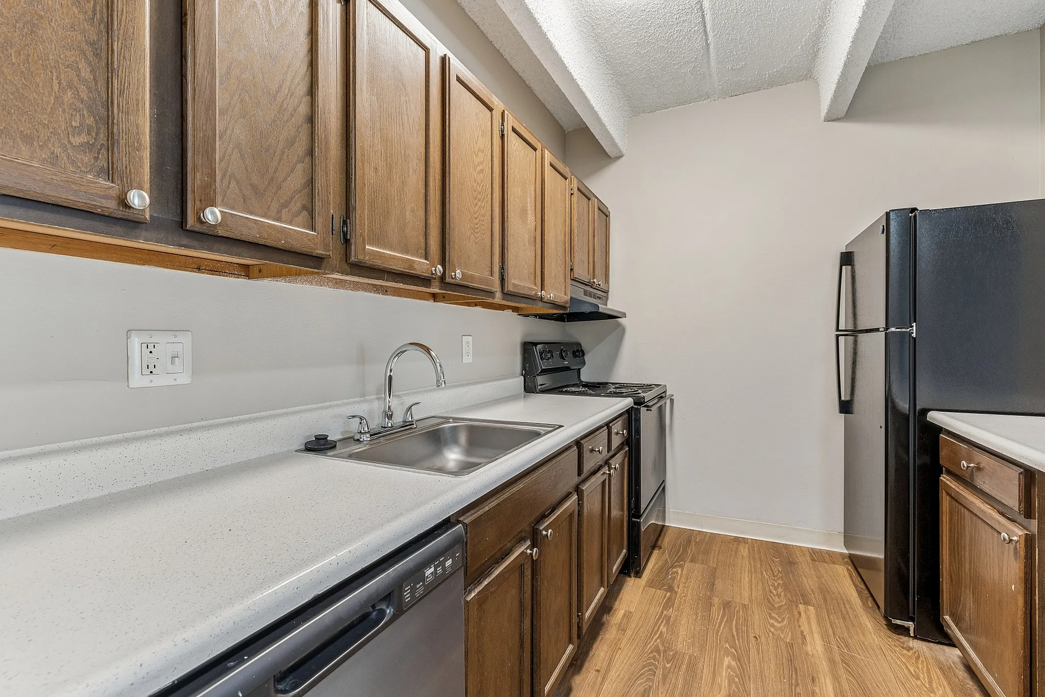 Modern kitchen with sleek countertops, dark wood cabinets, and stainless steel appliances under a beamed ceiling.