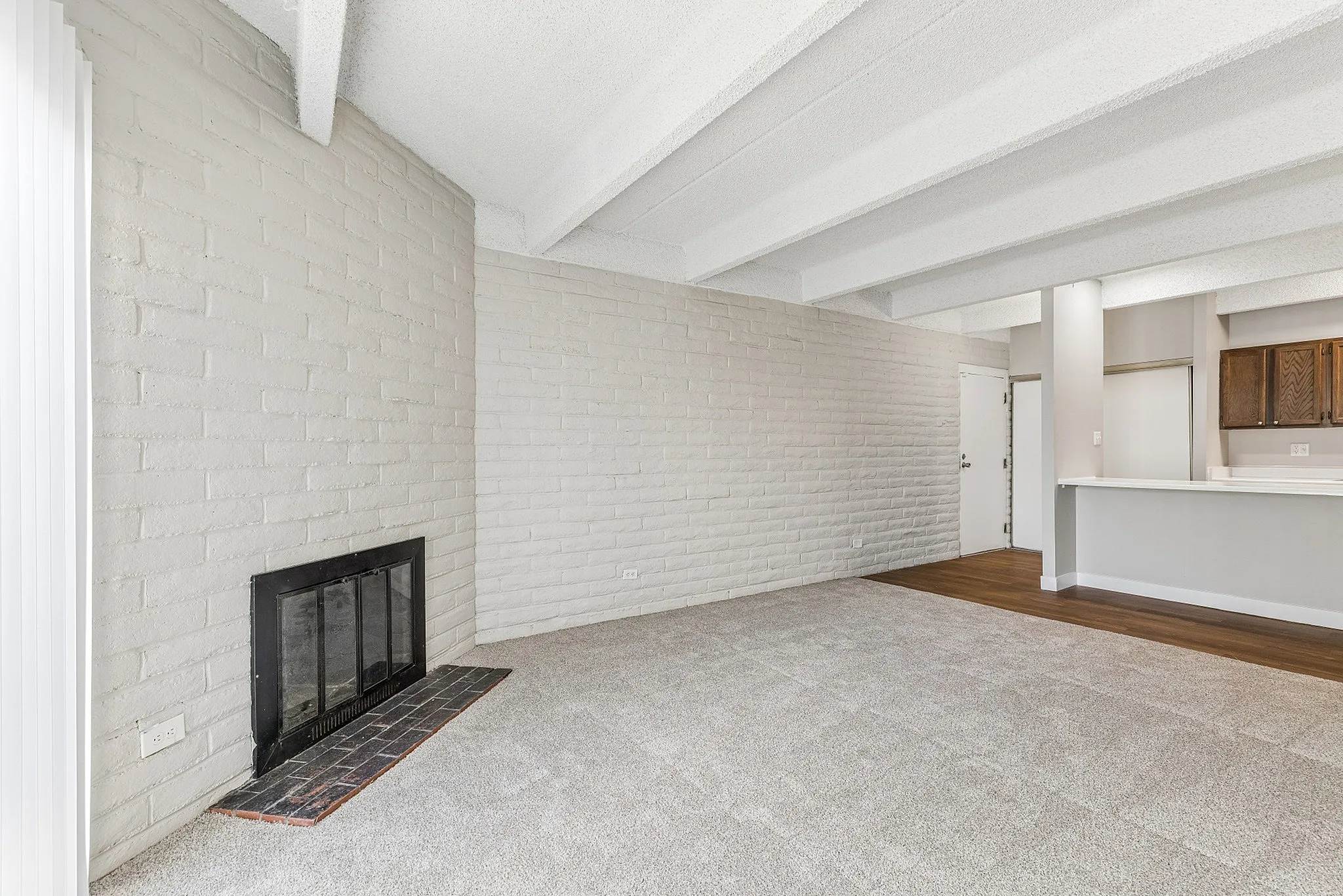 Bright and inviting living area with stylish brick accent wall, cozy fireplace, and seamless access to a sleek kitchen.
