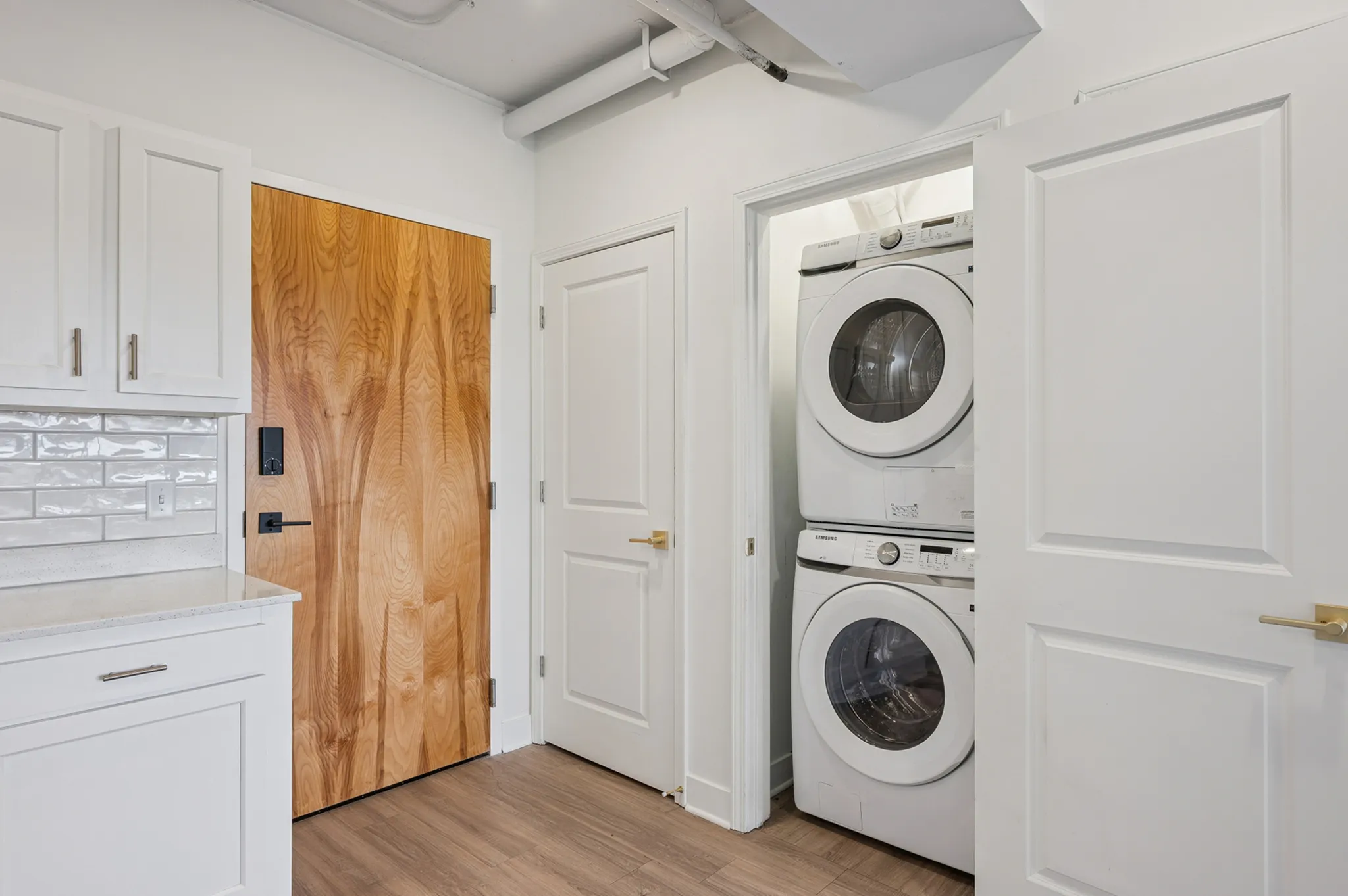 Chic apartment hallway showcasing sleek hardwood floors, elegant cabinetry, and a convenient in-unit stacked washer and dryer.